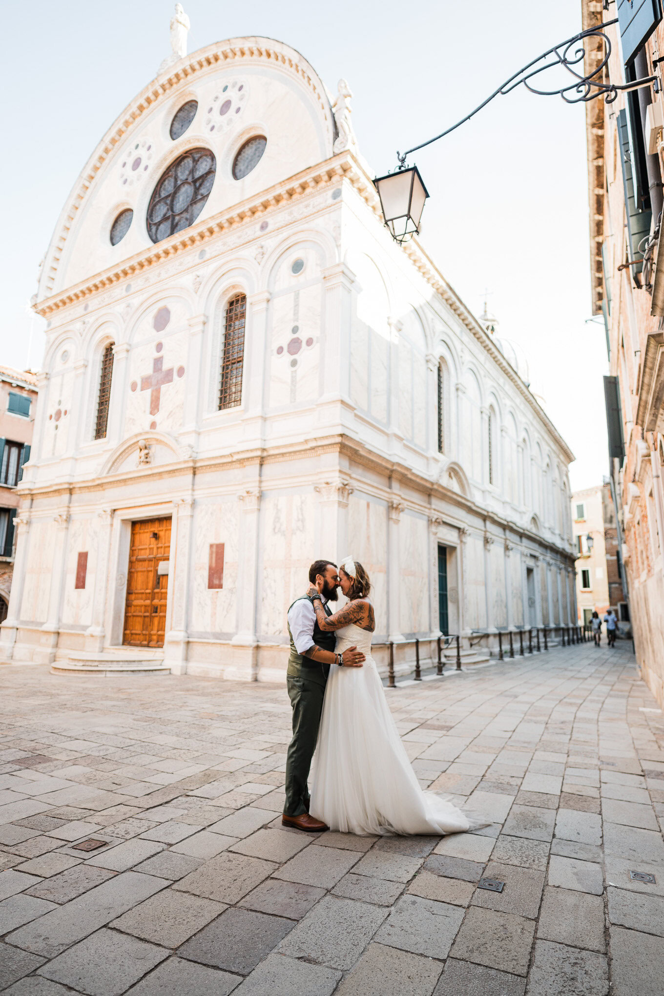 A couple sharing an intimate moment in front of a historic church in Venice, bathed in soft natural light, creating a ro.