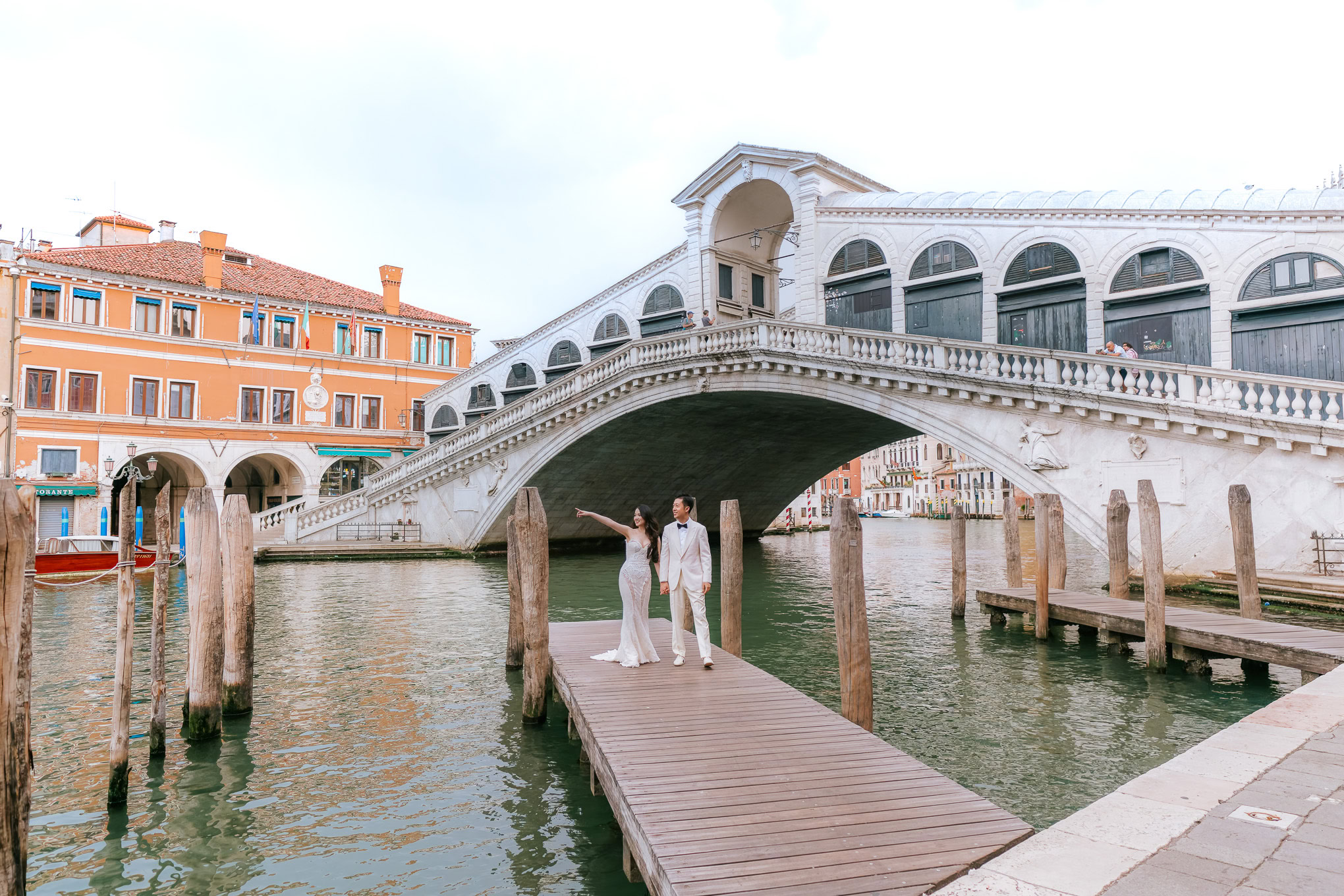 Romantic couple standing on a wooden dock beneath the Bridge of Sighs in Venice, bathed in soft natural light, creating.