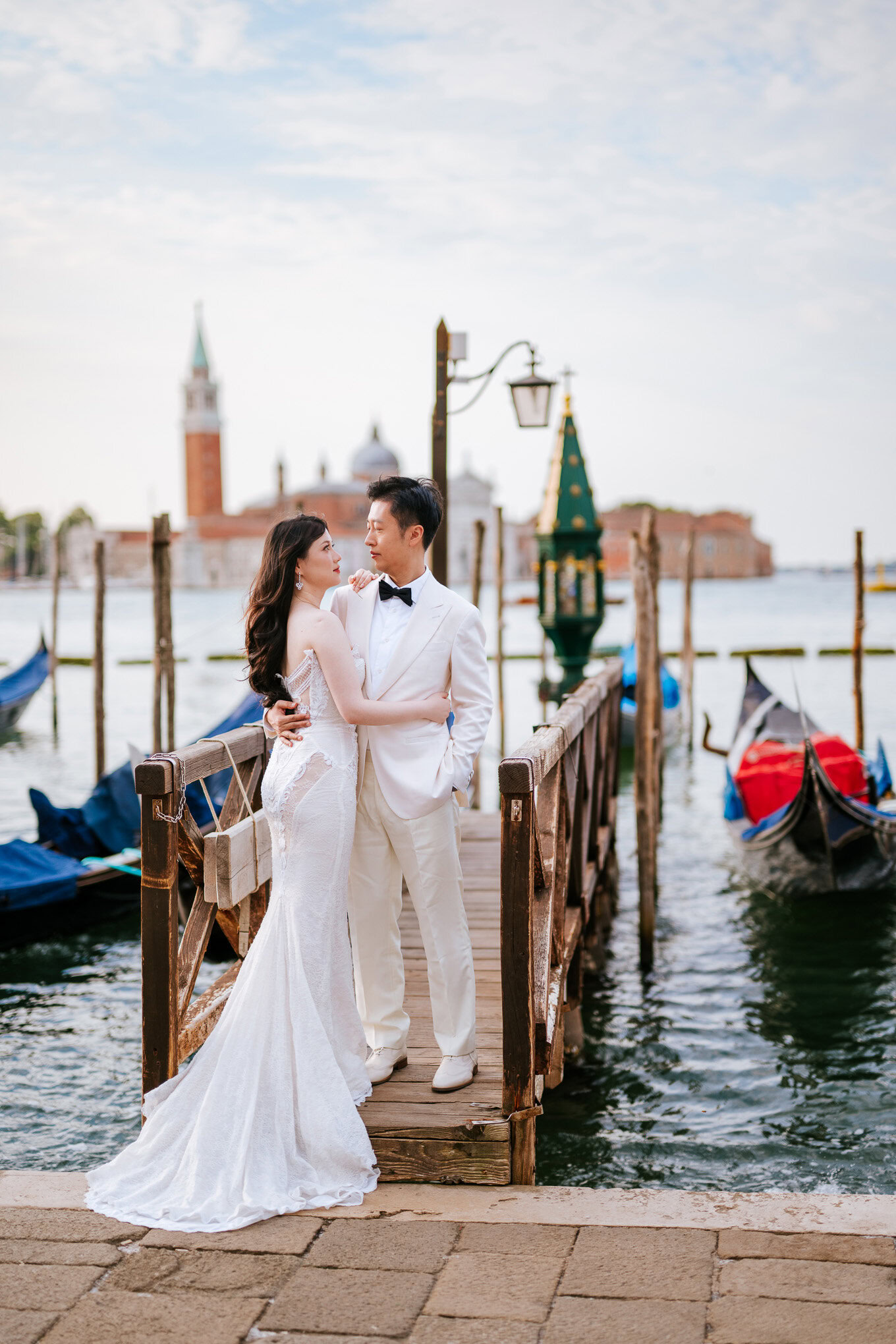 A couple in elegant attire sharing a romantic moment on a Venice dock with gondolas and historic architecture in.