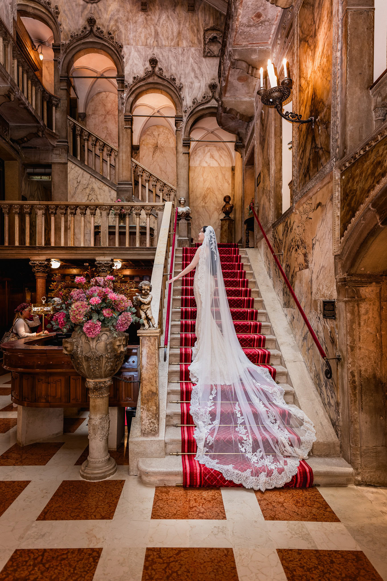 A couple in romantic embrace at the foot of a grand staircase inside an opulent Venetian palace, bathed in warm, golden.