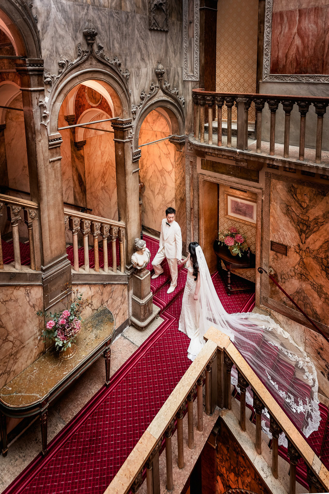 A woman in a wedding dress and a man in formal attire in an ornate Venetian interior with marble walls and decorative ar.