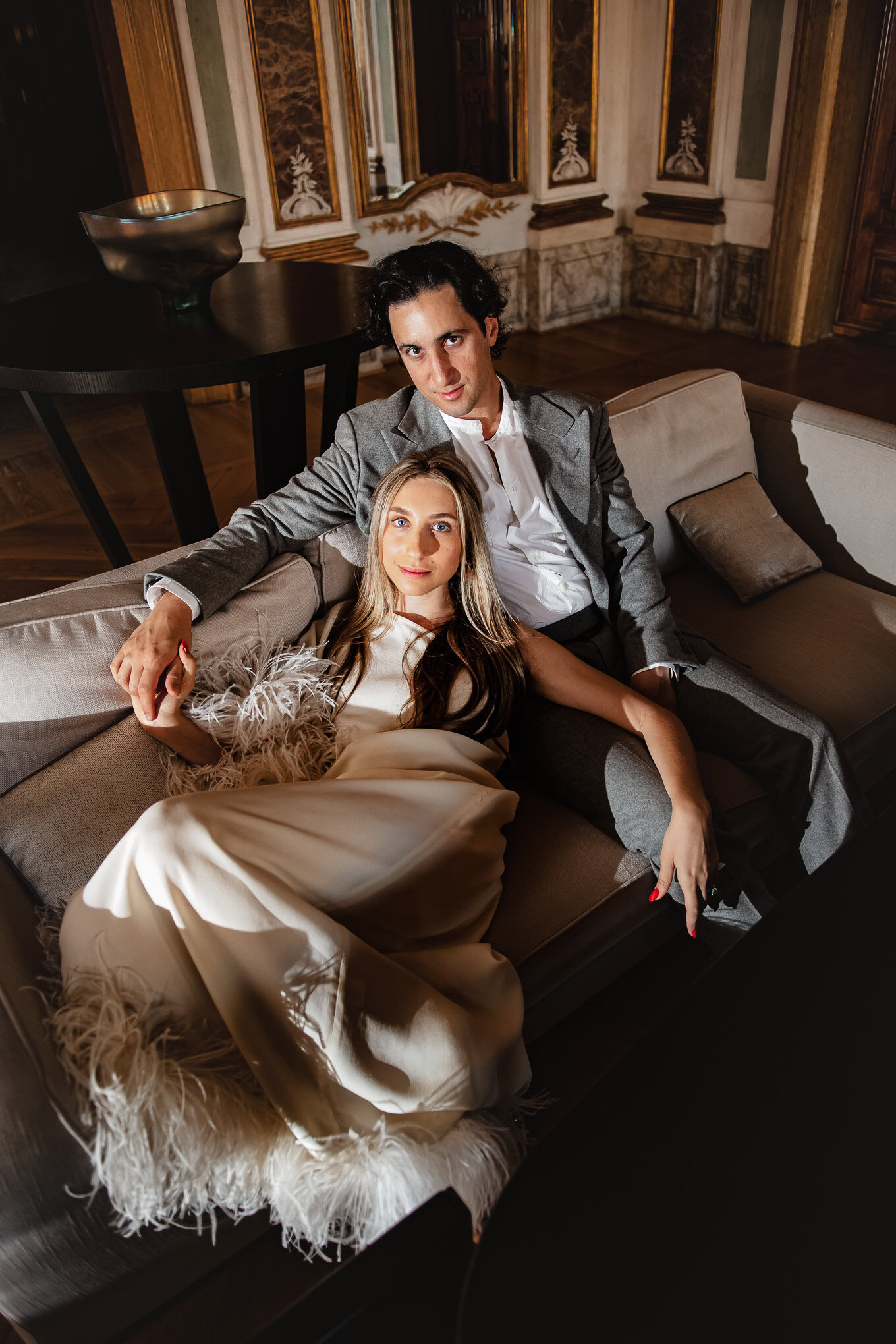 A couple relaxing on a luxurious sofa in an elegant Venetian interior, basking in warm, romantic light.