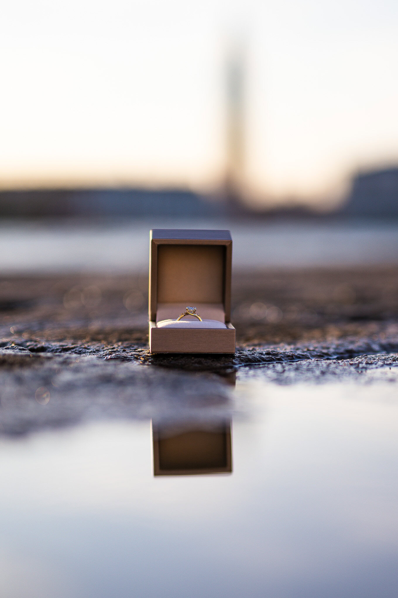 An engaged couple's ring box is placed on the wet ground near the Venice waterfront at sunset, capturing a romantic prop.