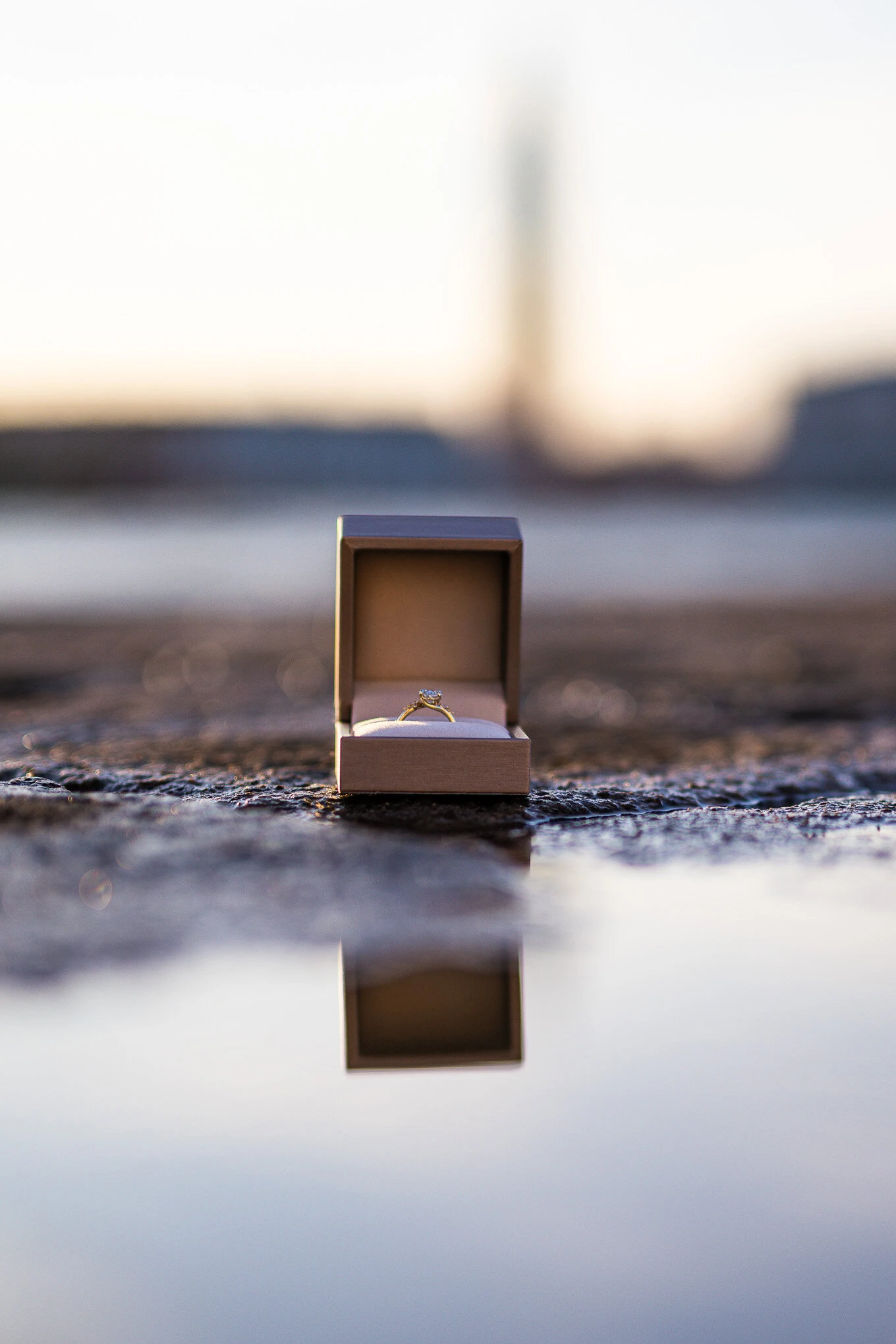 An engaged couple's ring box is placed on the wet ground near the Venice waterfront at sunset, capturing a romantic prop.
