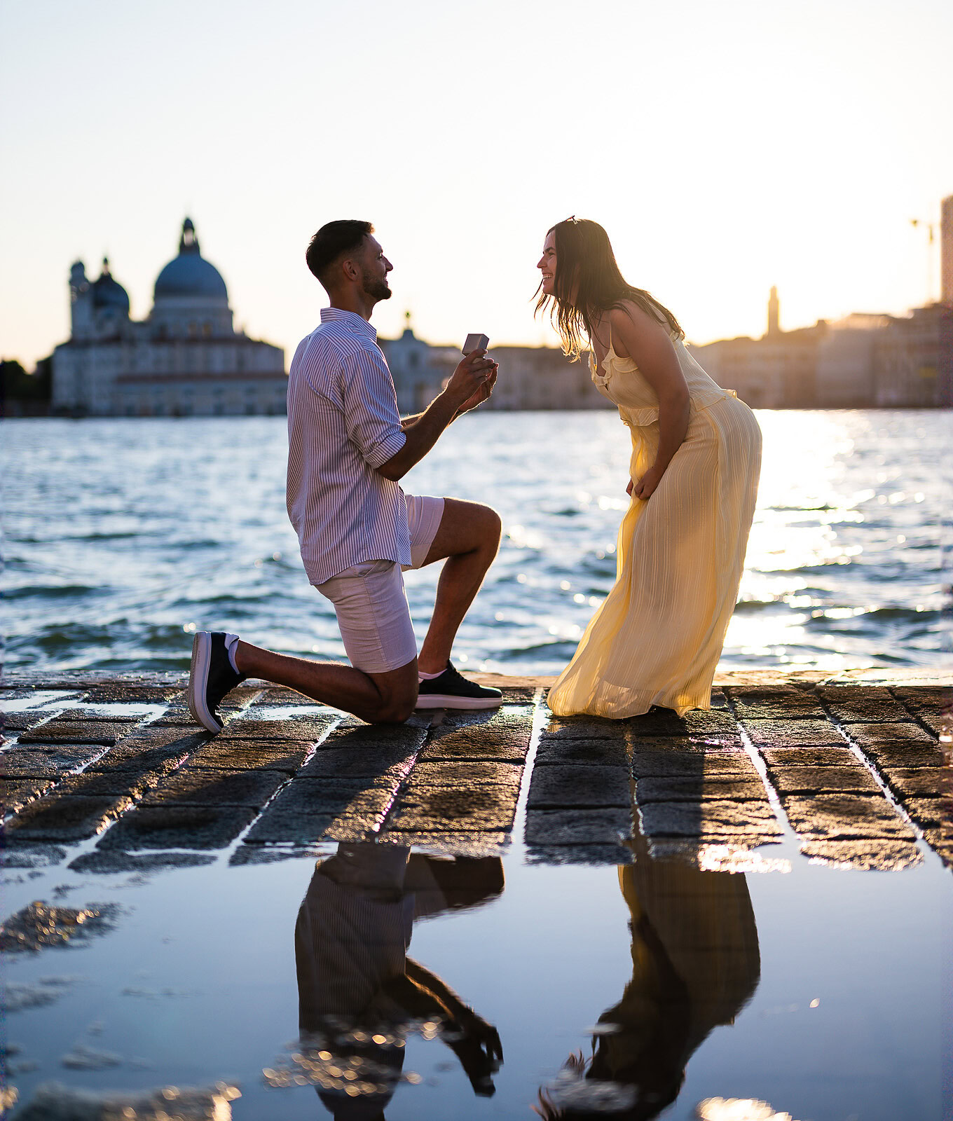 A man proposes to a woman on a Venice waterfront at sunset, capturing a heartfelt moment of love and commitment.