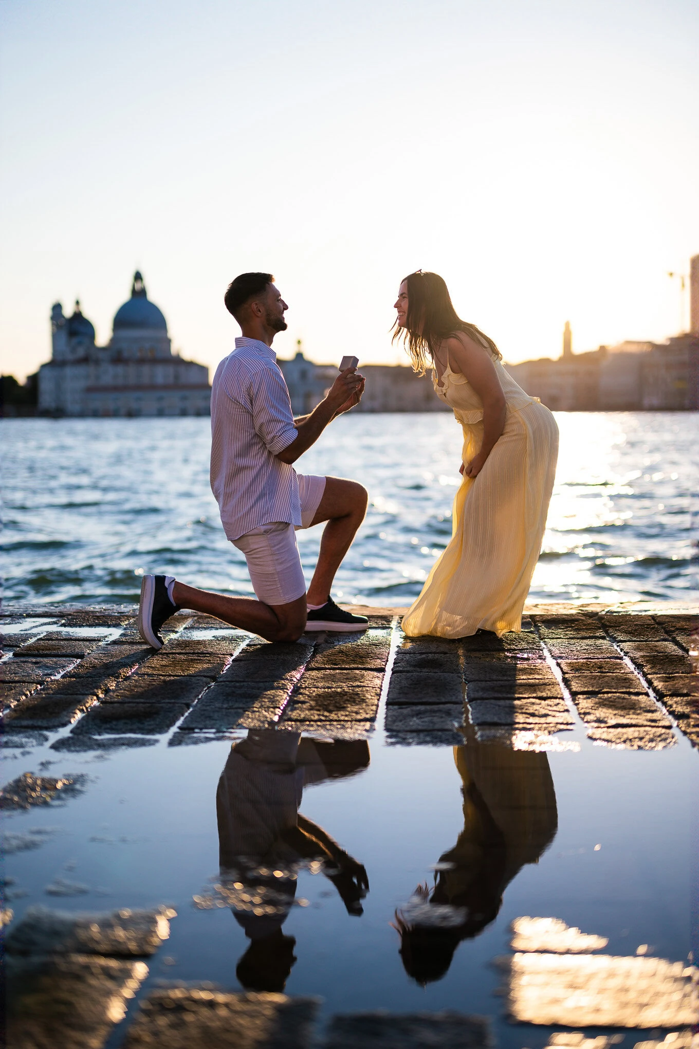 A man proposes to a woman on a Venice waterfront at sunset, capturing a heartfelt moment of love and commitment.