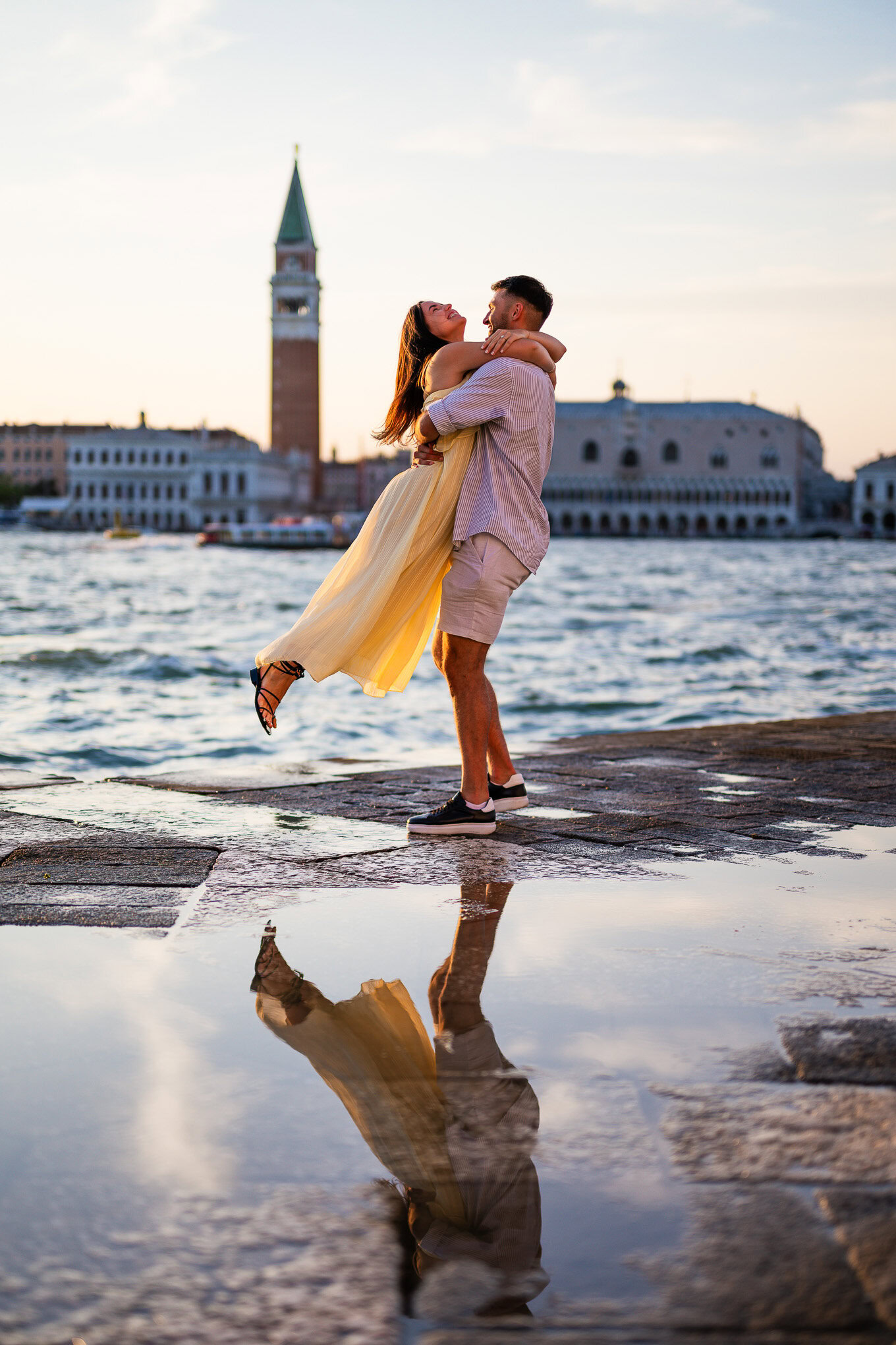 A couple shares a romantic proposal moment by the Venice canal, embracing passionately as the sunset reflects on the wat.