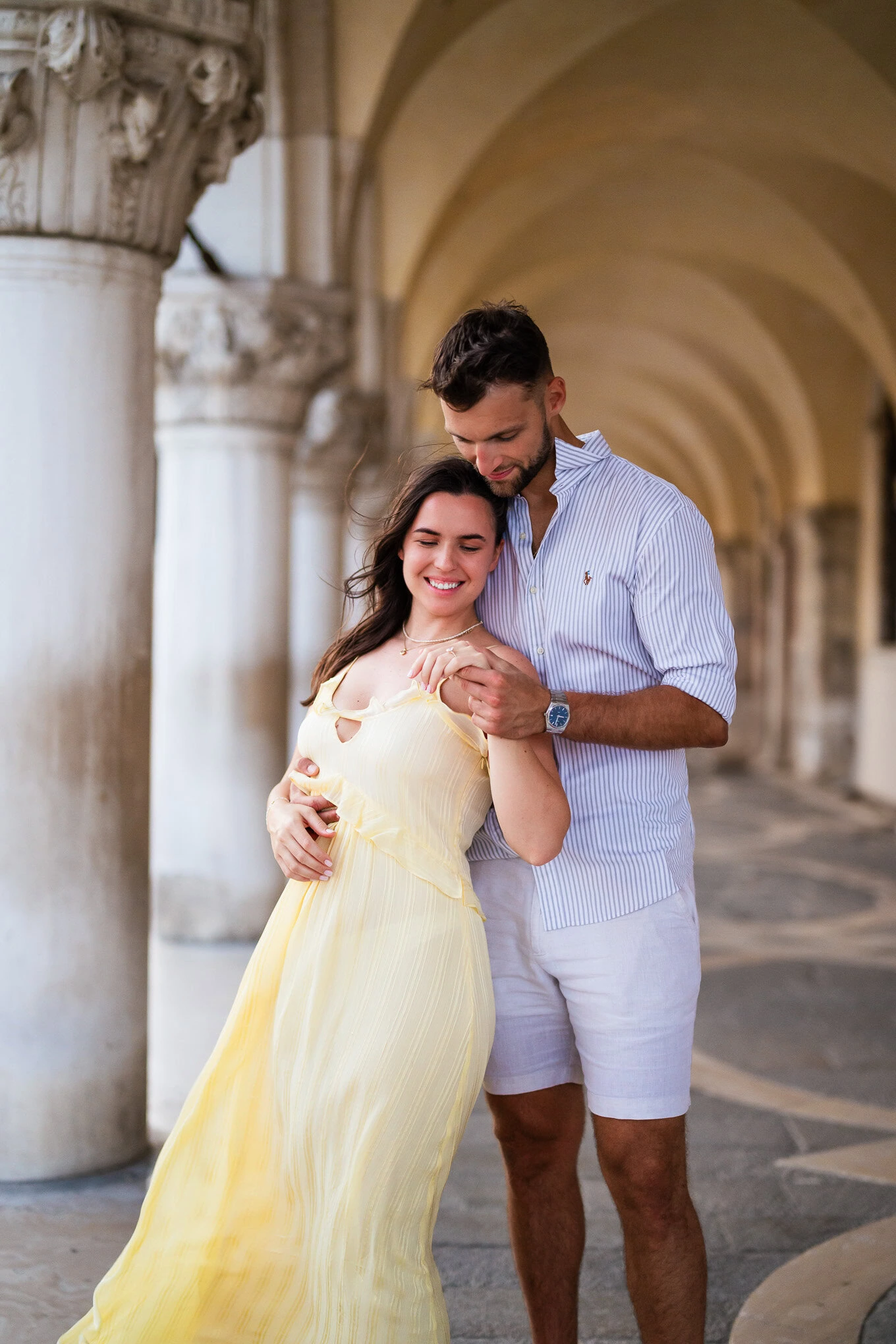 A couple shares an emotional proposal moment under Venice's historic arches, capturing love and joy in a candid gesture.