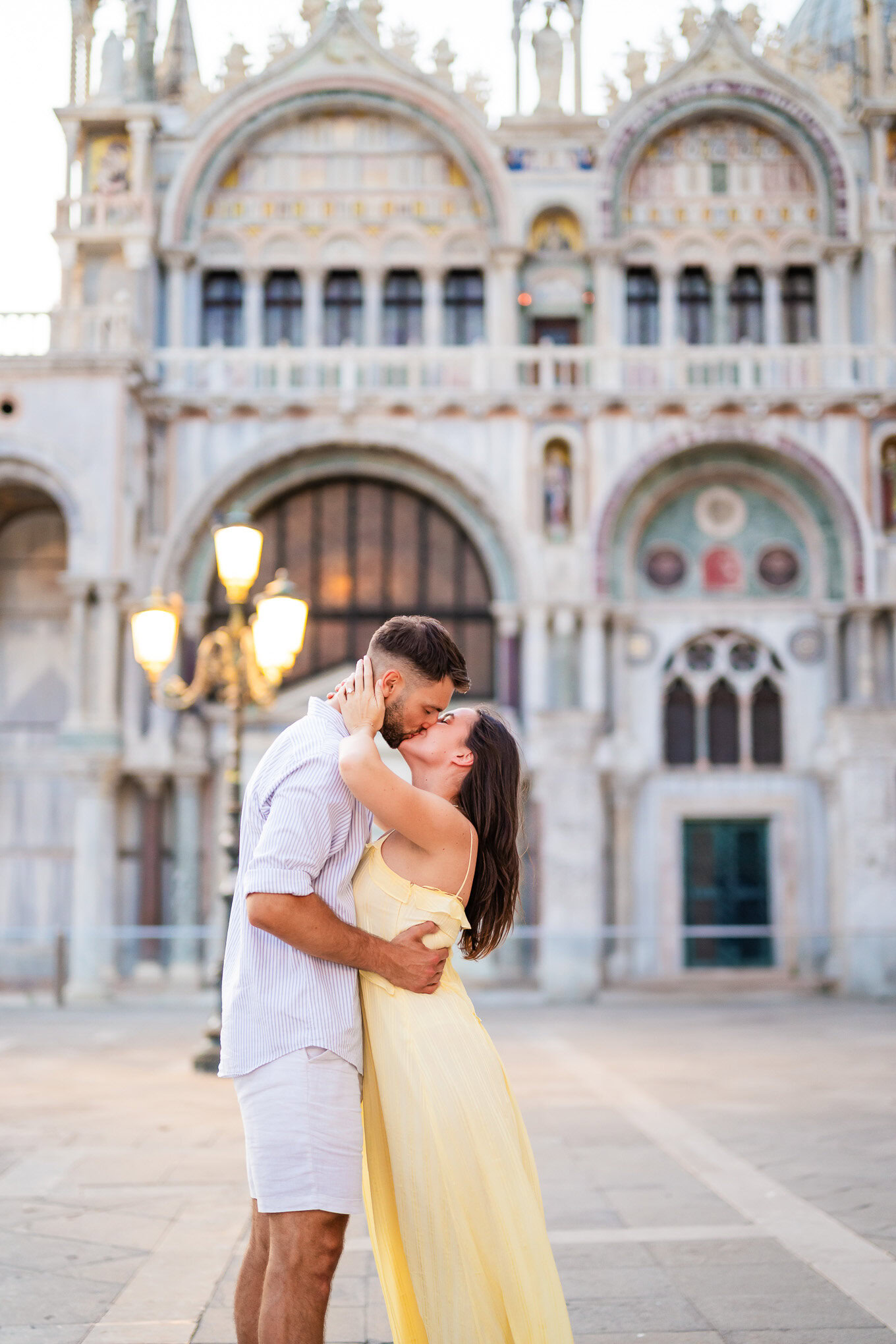 A couple embracing and kissing in front of a historic Venetian cathedral, capturing a romantic and atmospheric scene.