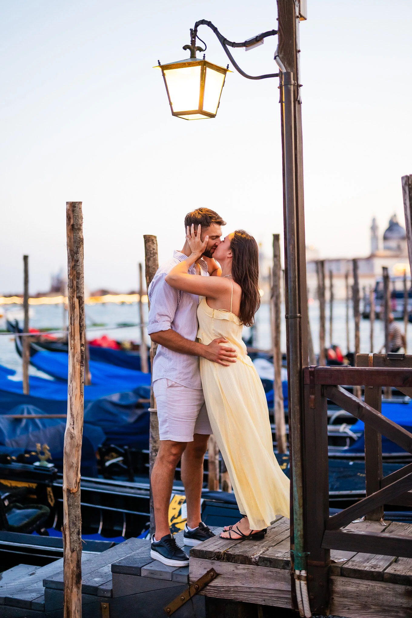 A couple shares a heartfelt proposal kiss on a Venice dock, capturing a moment of love and joy by the water.