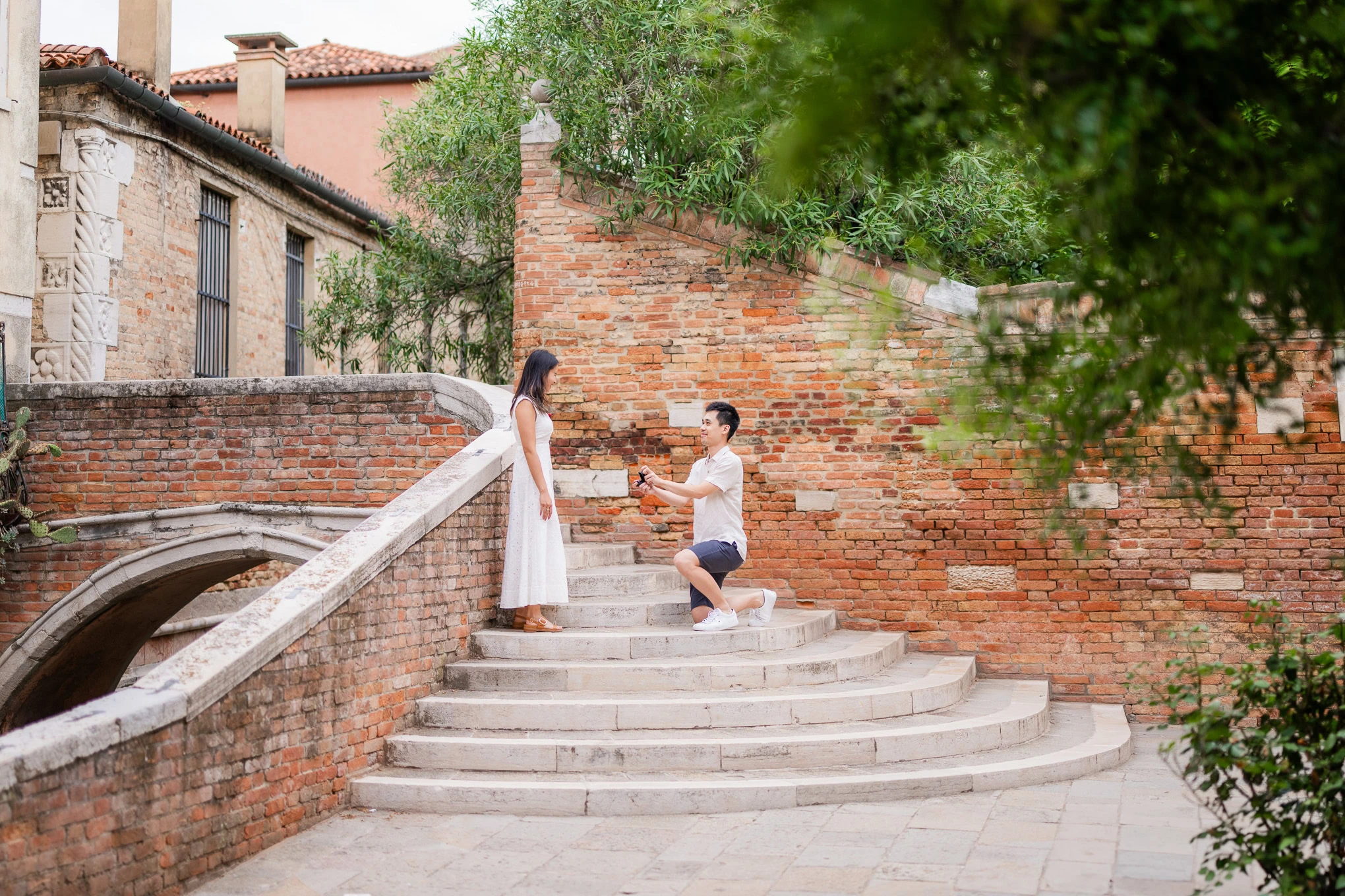 A woman reacts with surprise as a man kneels proposing on a charming Venice staircase.