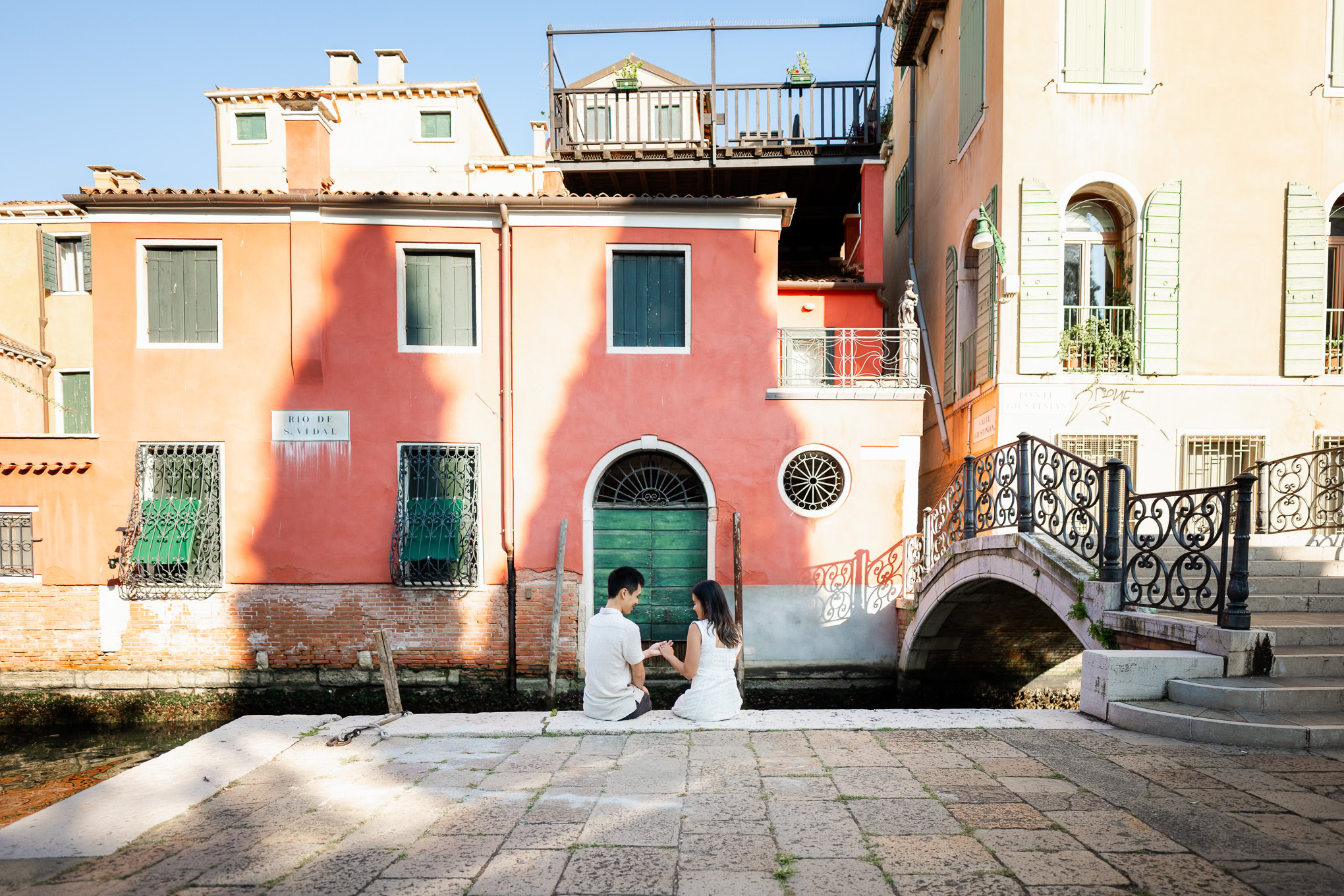 A couple shares a romantic proposal moment by the canal in Venice, with vibrant buildings as a picturesque backdrop.