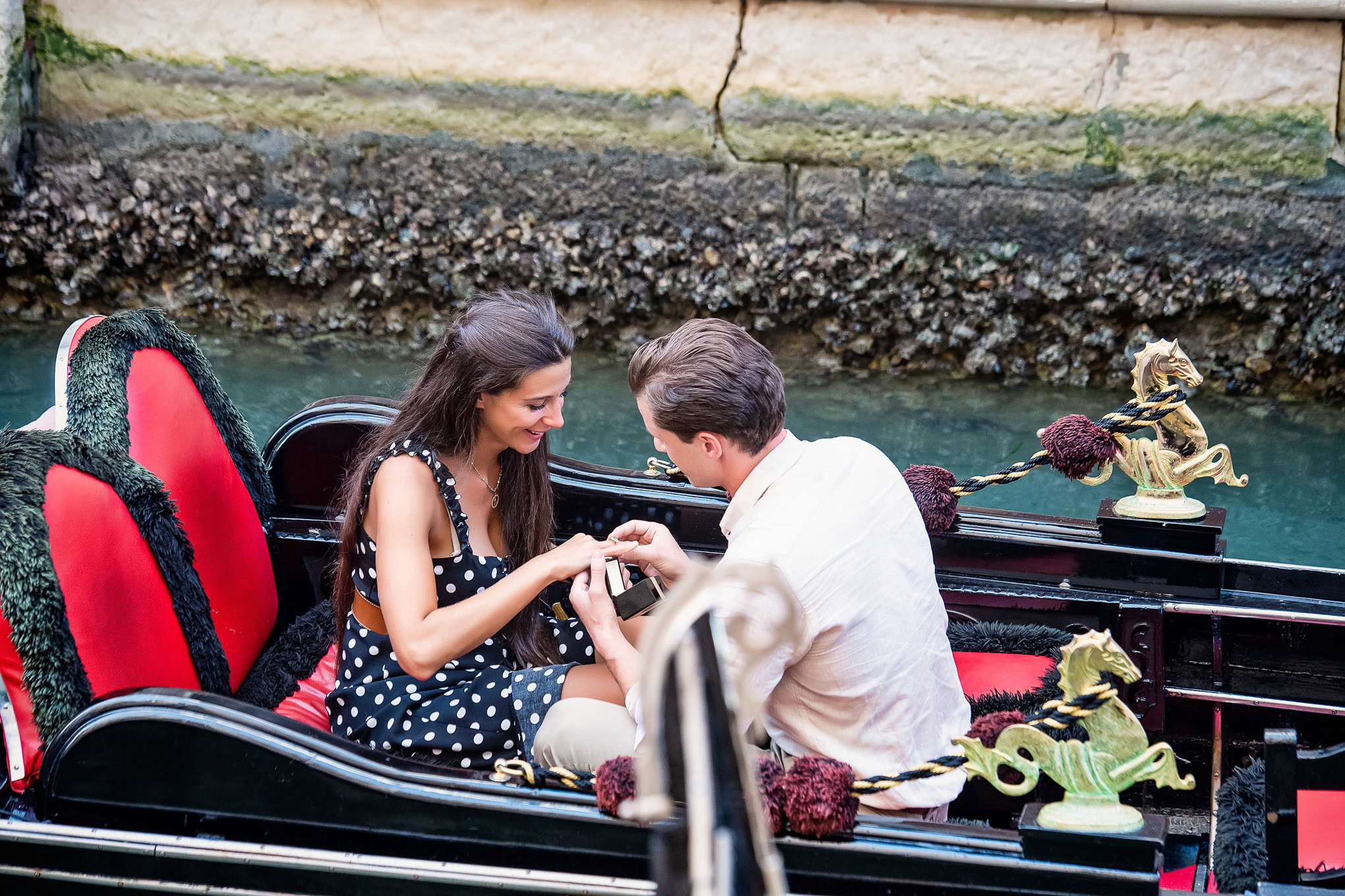 Two people enjoying a romantic gondola ride on a Venetian canal with historic architecture in the background.