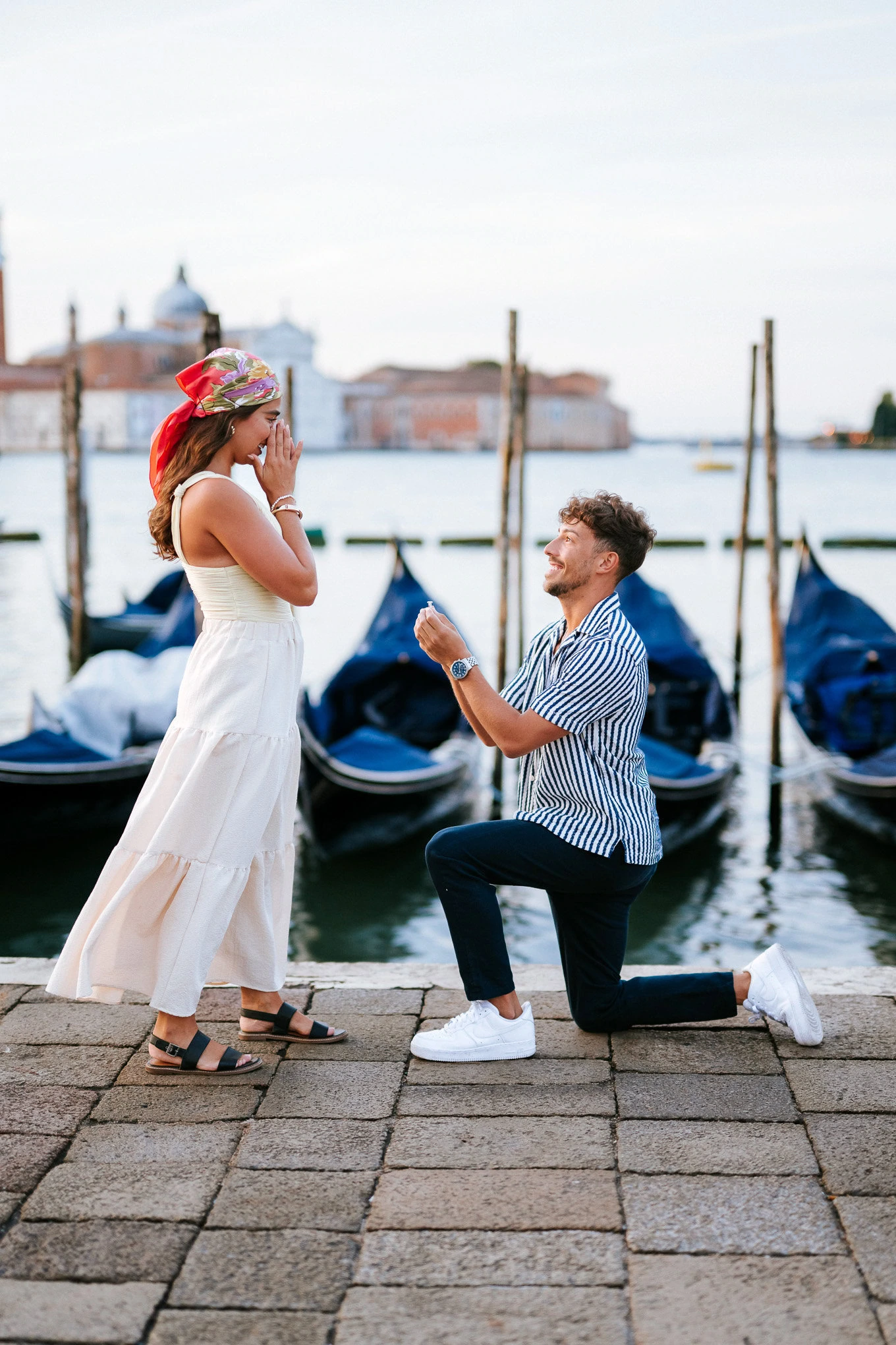 A woman reacts emotionally as a man kneels proposing with a ring by the Venetian canal.