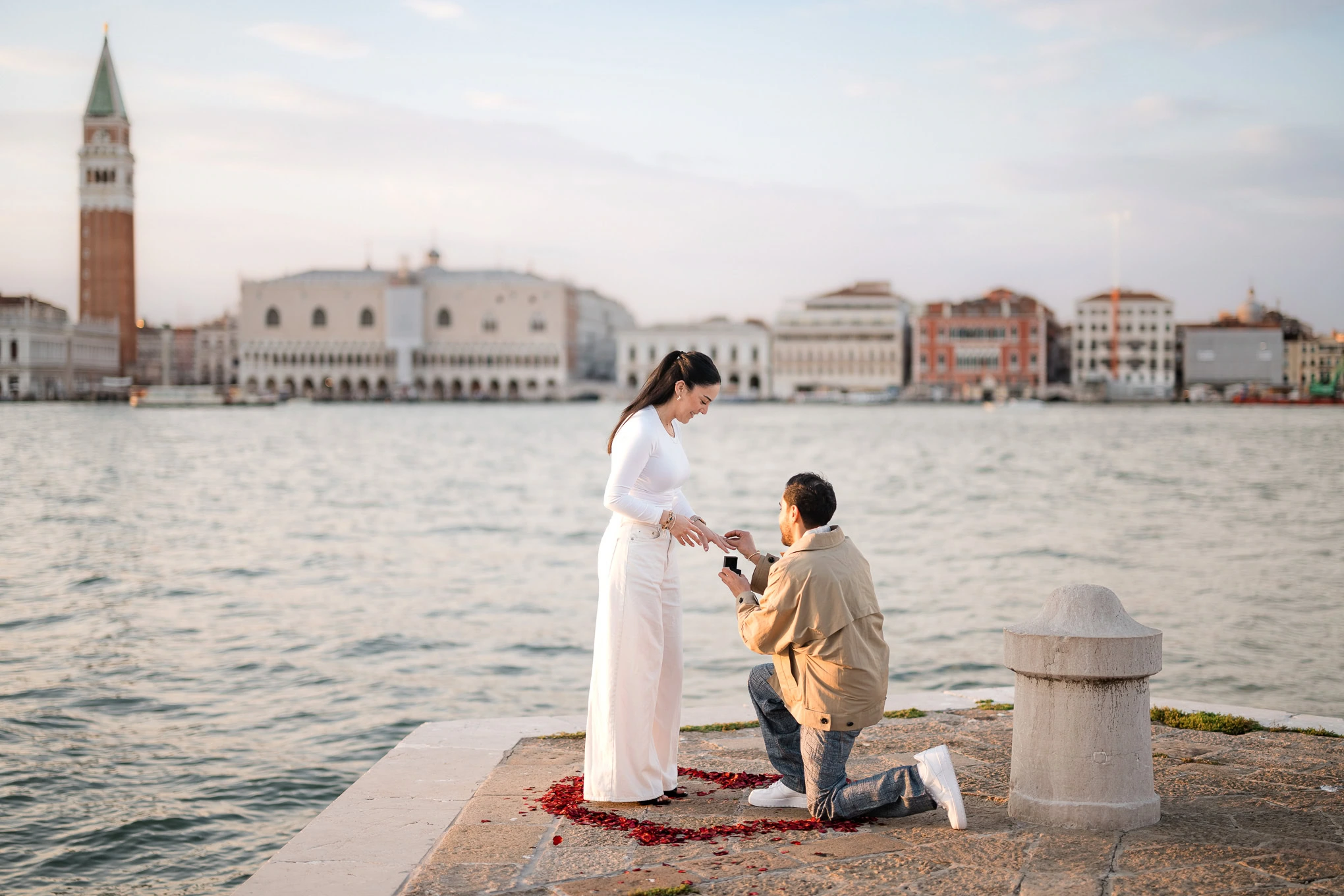A woman proposes to her partner on a Venice waterfront, capturing a heartfelt moment of love and commitment.