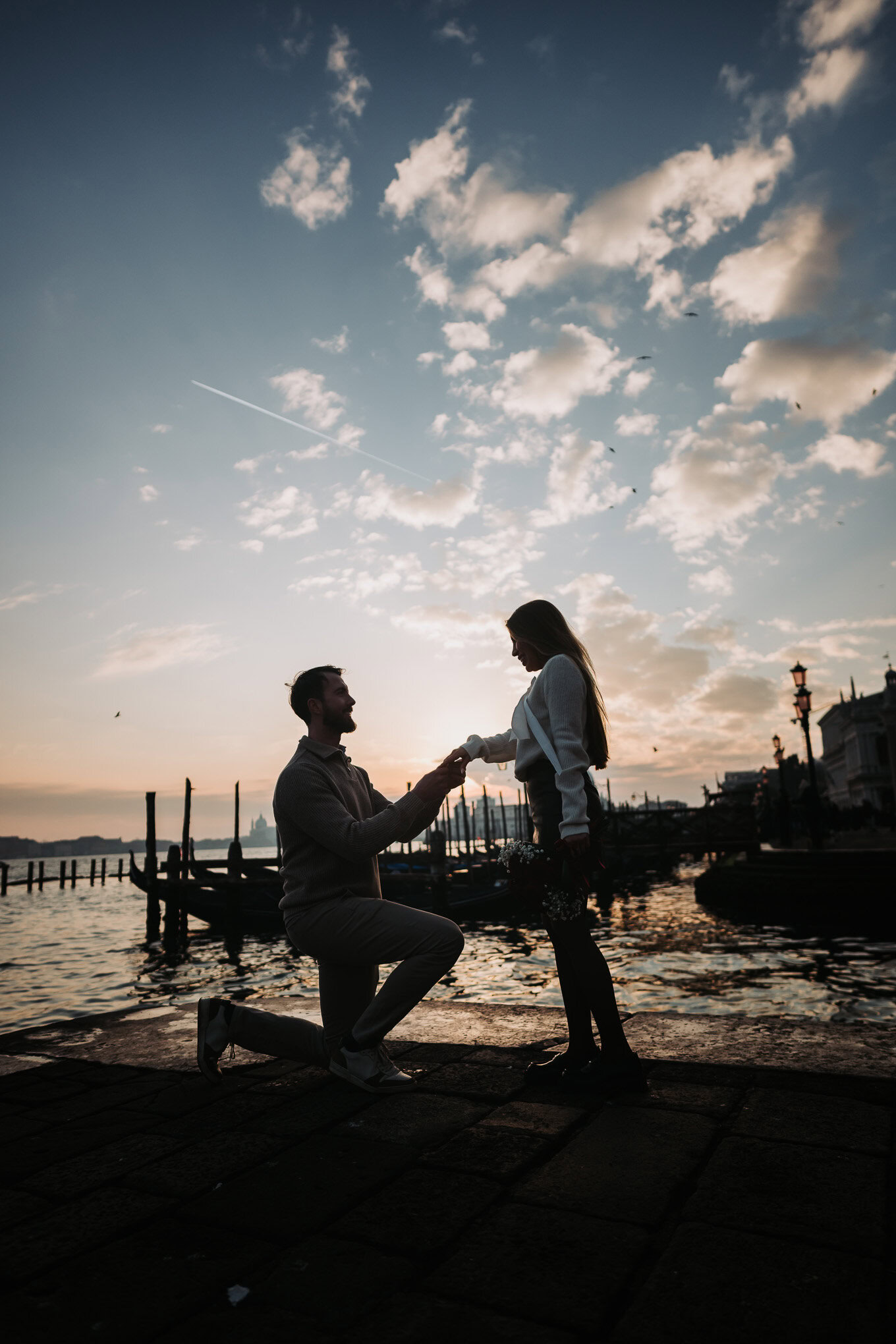 A man proposes to a woman on a Venice waterfront at sunset, capturing a heartfelt moment of love and commitment.