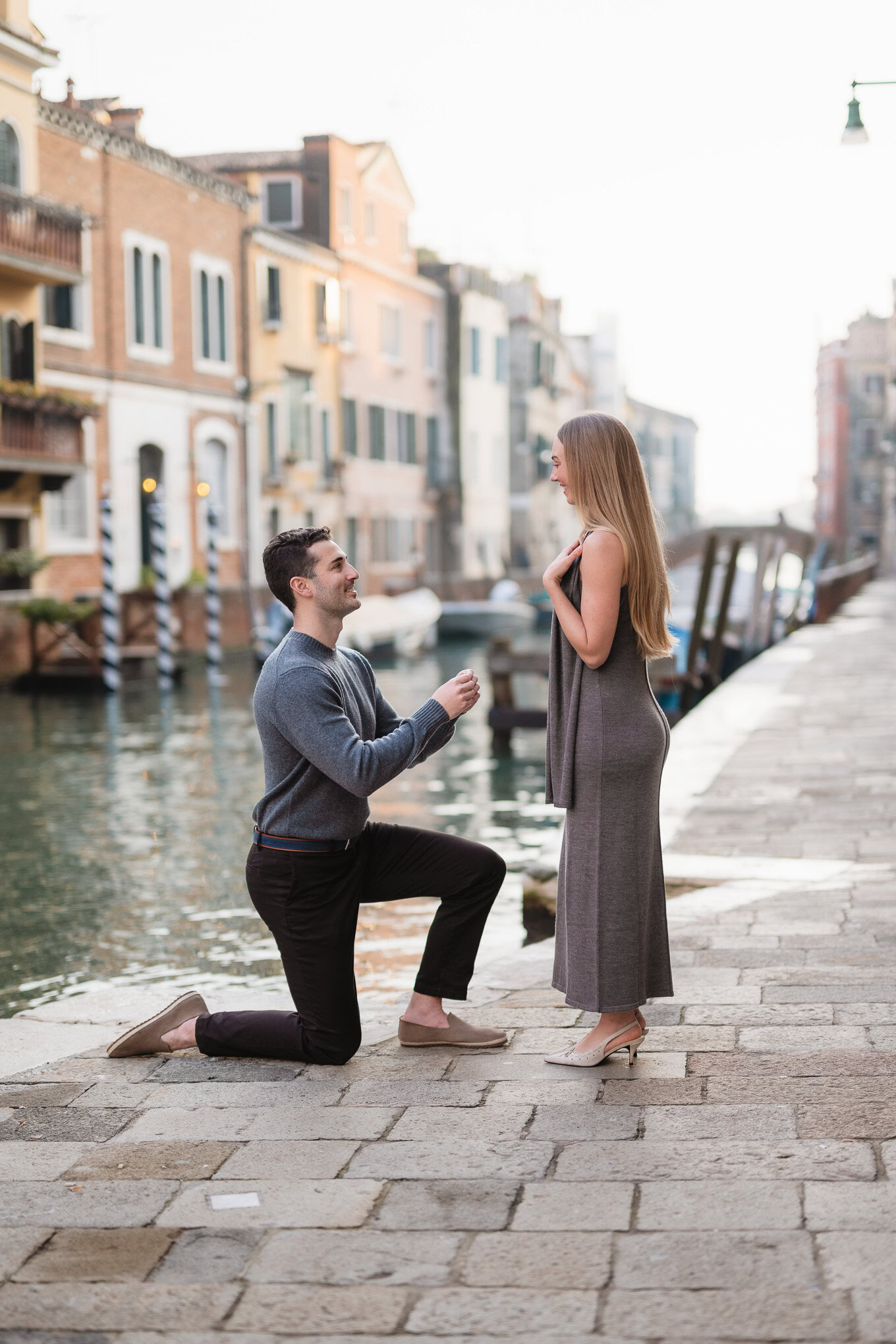 A man proposes to a woman on a Venice canal promenade, capturing a heartfelt moment filled with emotion and anticipation.