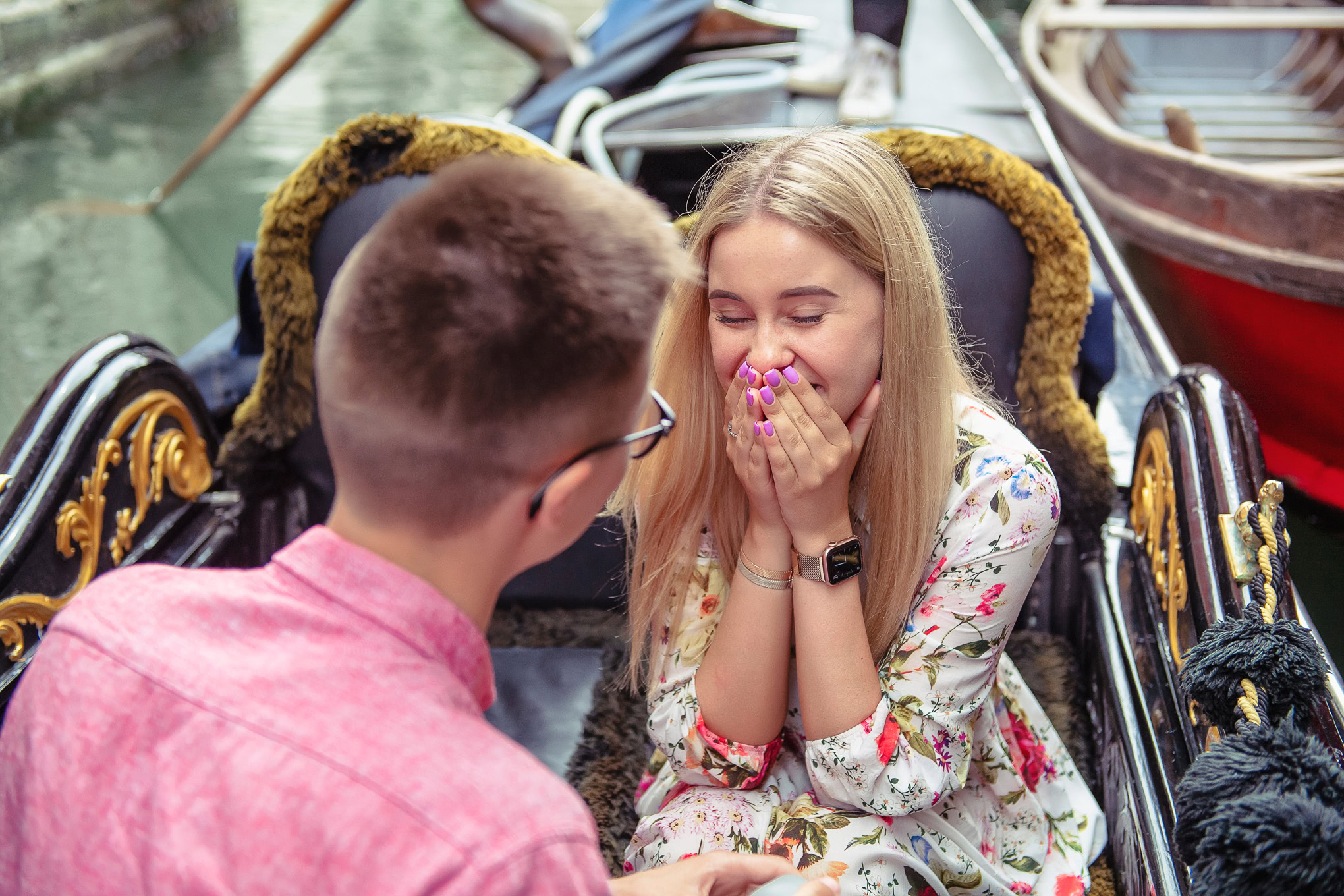 A woman reacts joyfully as her partner proposes on a gondola in Venice, capturing a heartfelt moment of love and surpris.