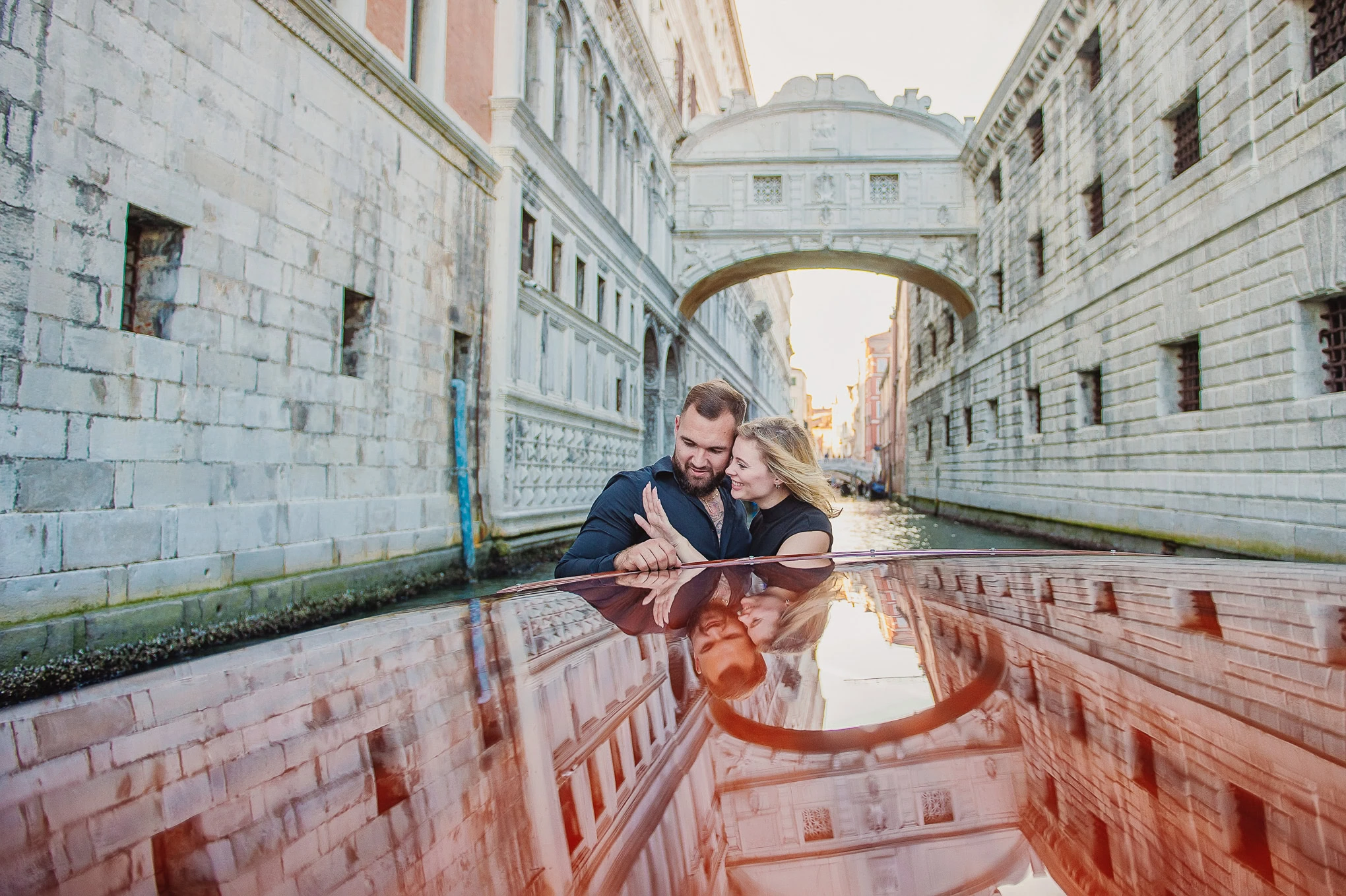 A couple shares an emotional proposal moment in Venice, with the man kneeling and the woman reacting with surprise and j.