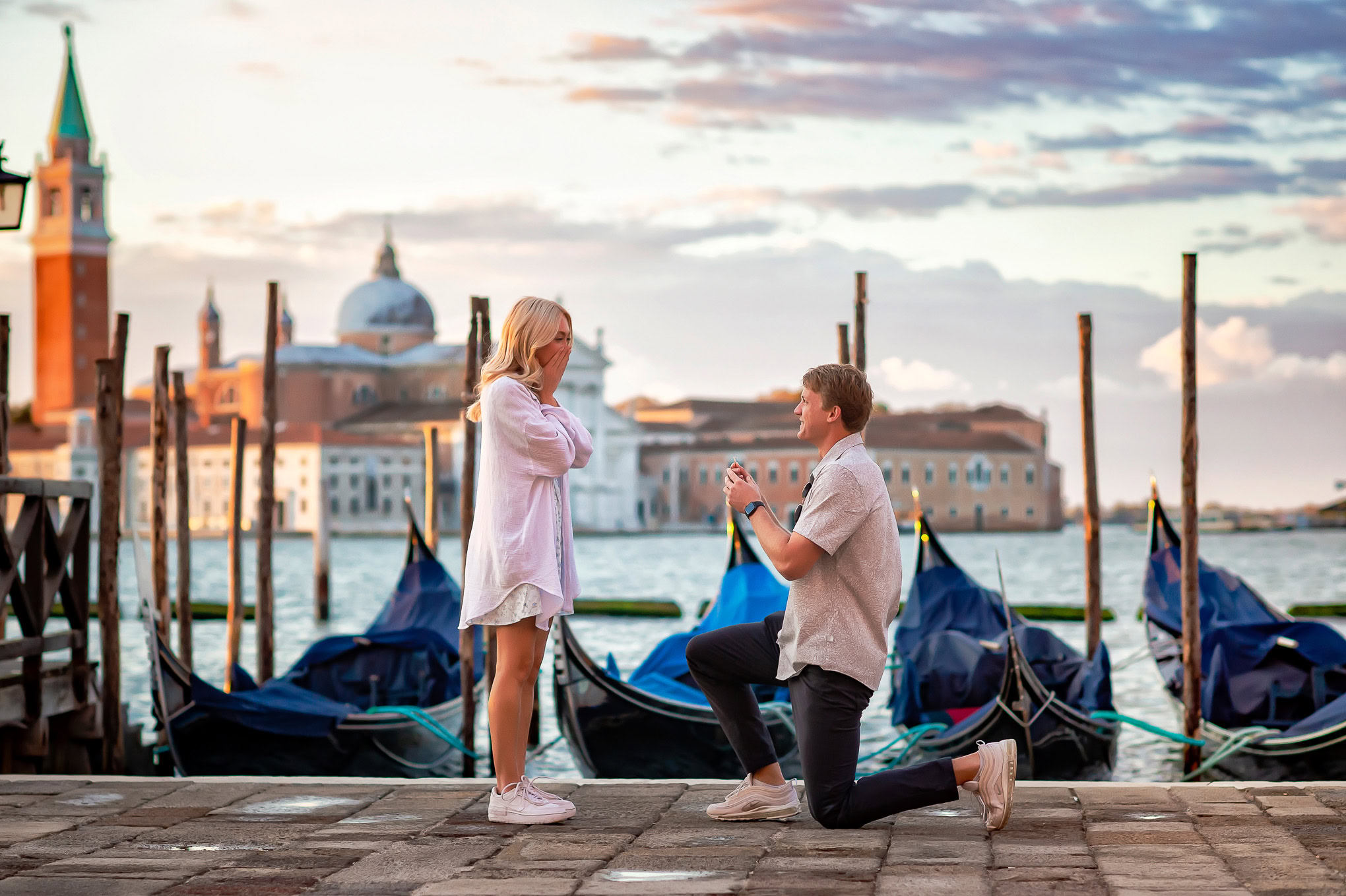 A woman and man on a Venice waterfront scene with gondolas and historic buildings in the background.