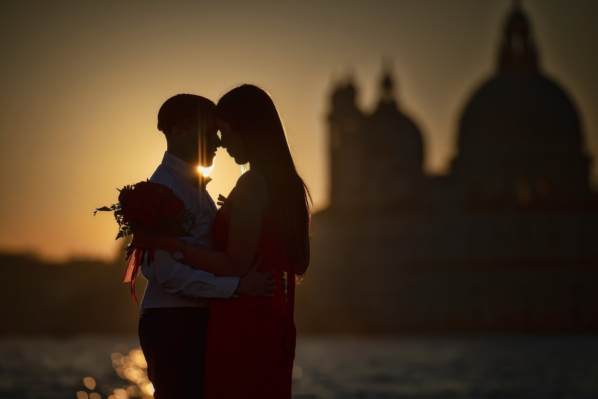 A couple shares a heartfelt proposal at sunset with Venice's skyline in the background.