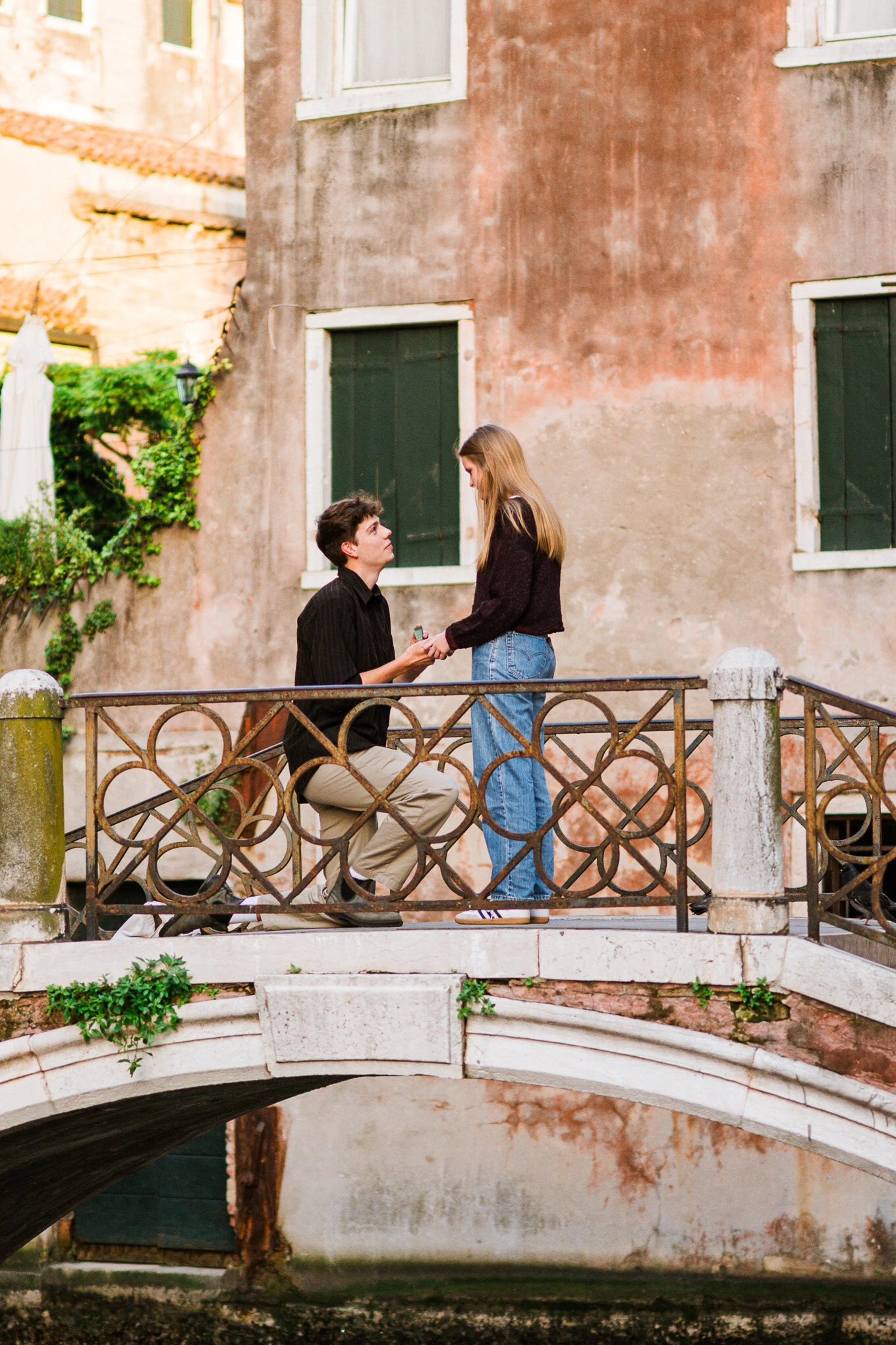 A man proposes to a woman on a small Venetian bridge, capturing a heartfelt moment of love and commitment.