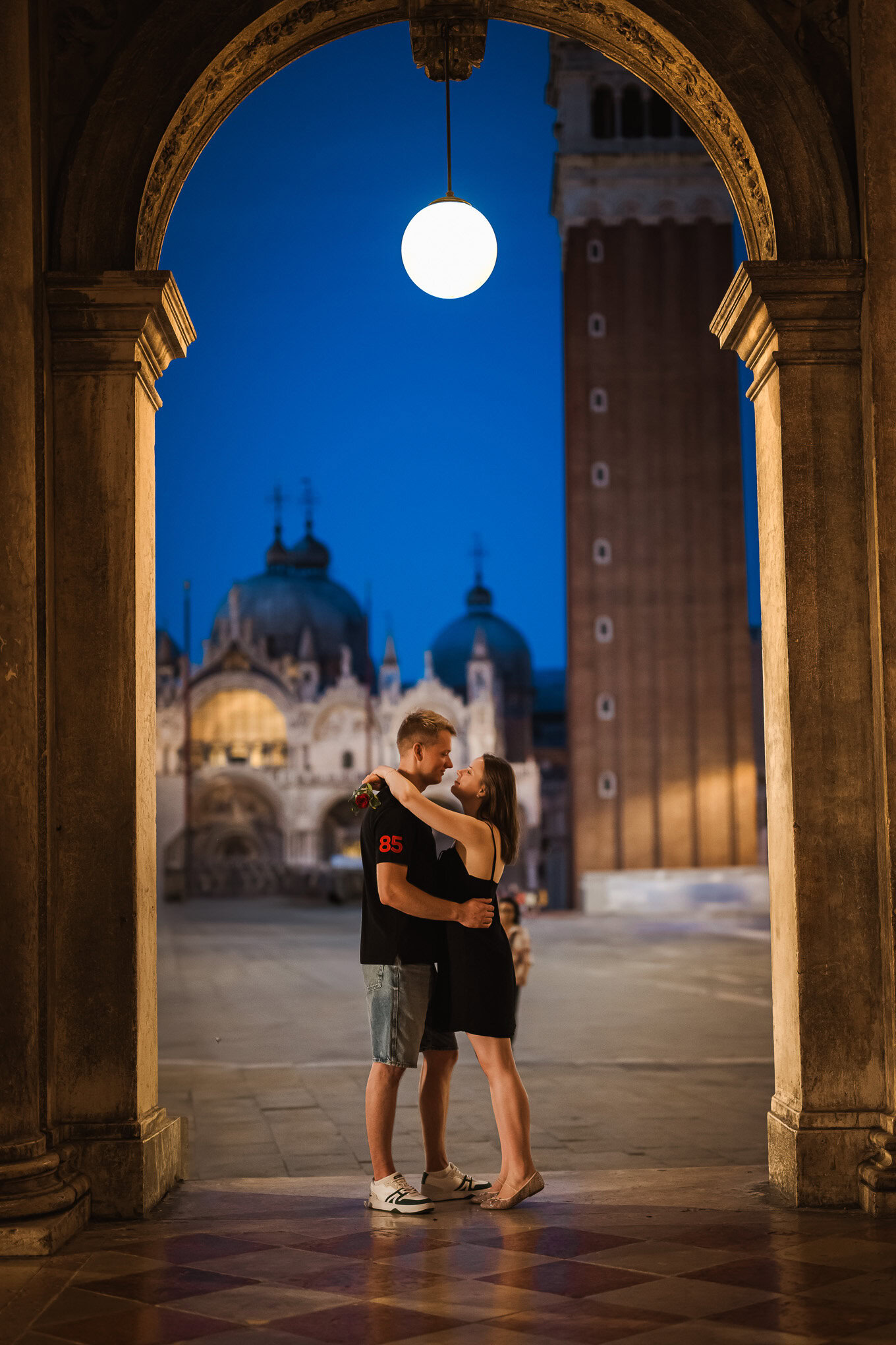 A couple shares a heartfelt proposal under a glowing lantern in Venice’s historic archway.