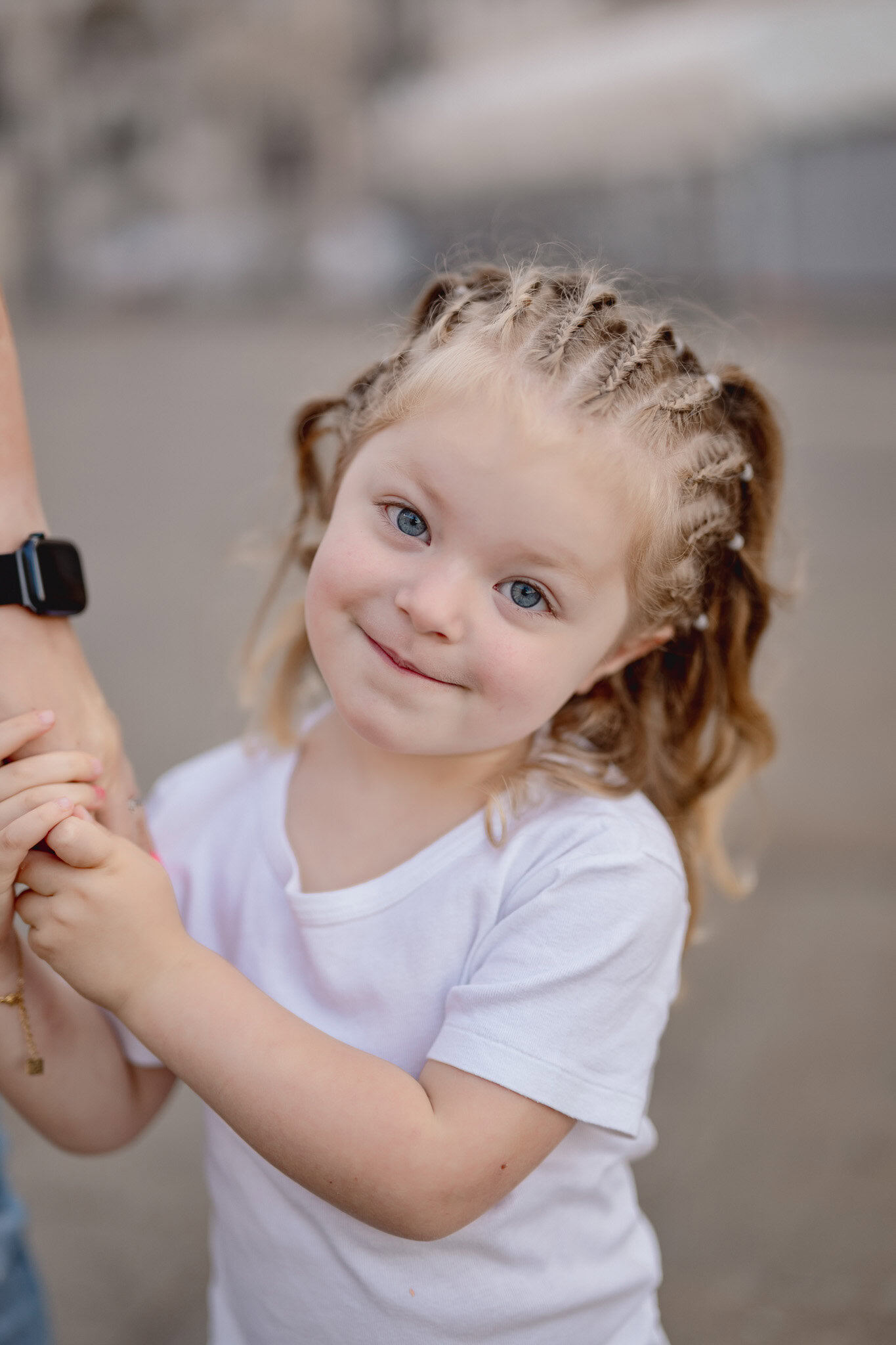 A girl with braided hair and blue eyes holding an adult's hand in San Marco Square, Venice.