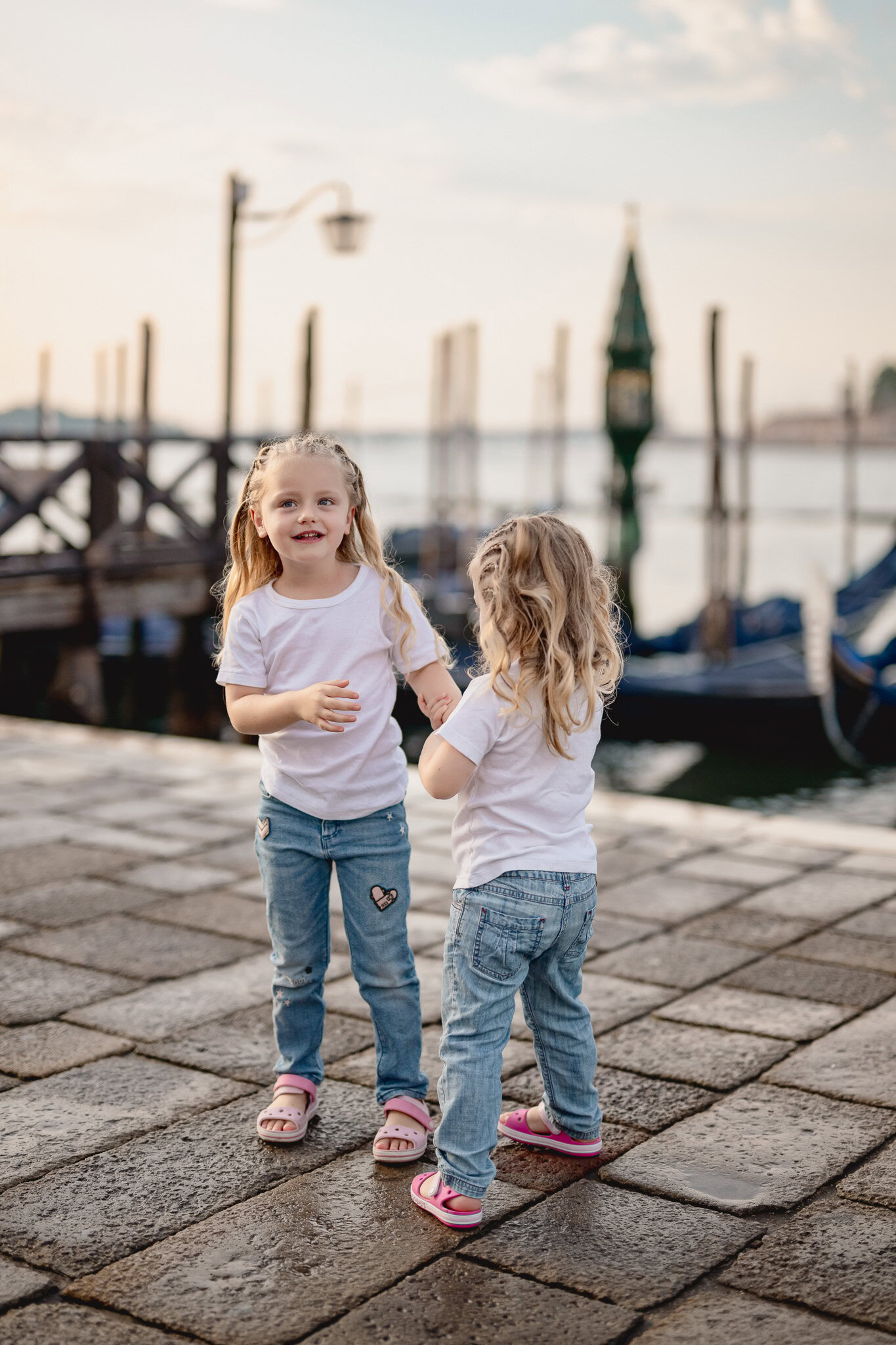 Children playing and holding hands near a waterfront with boats and historic architecture in the bac.