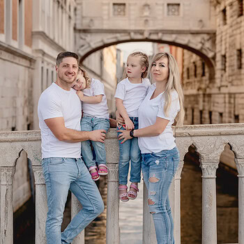 Family standing on a bridge in San Marco Square, Venice, with historic buildings in the background.