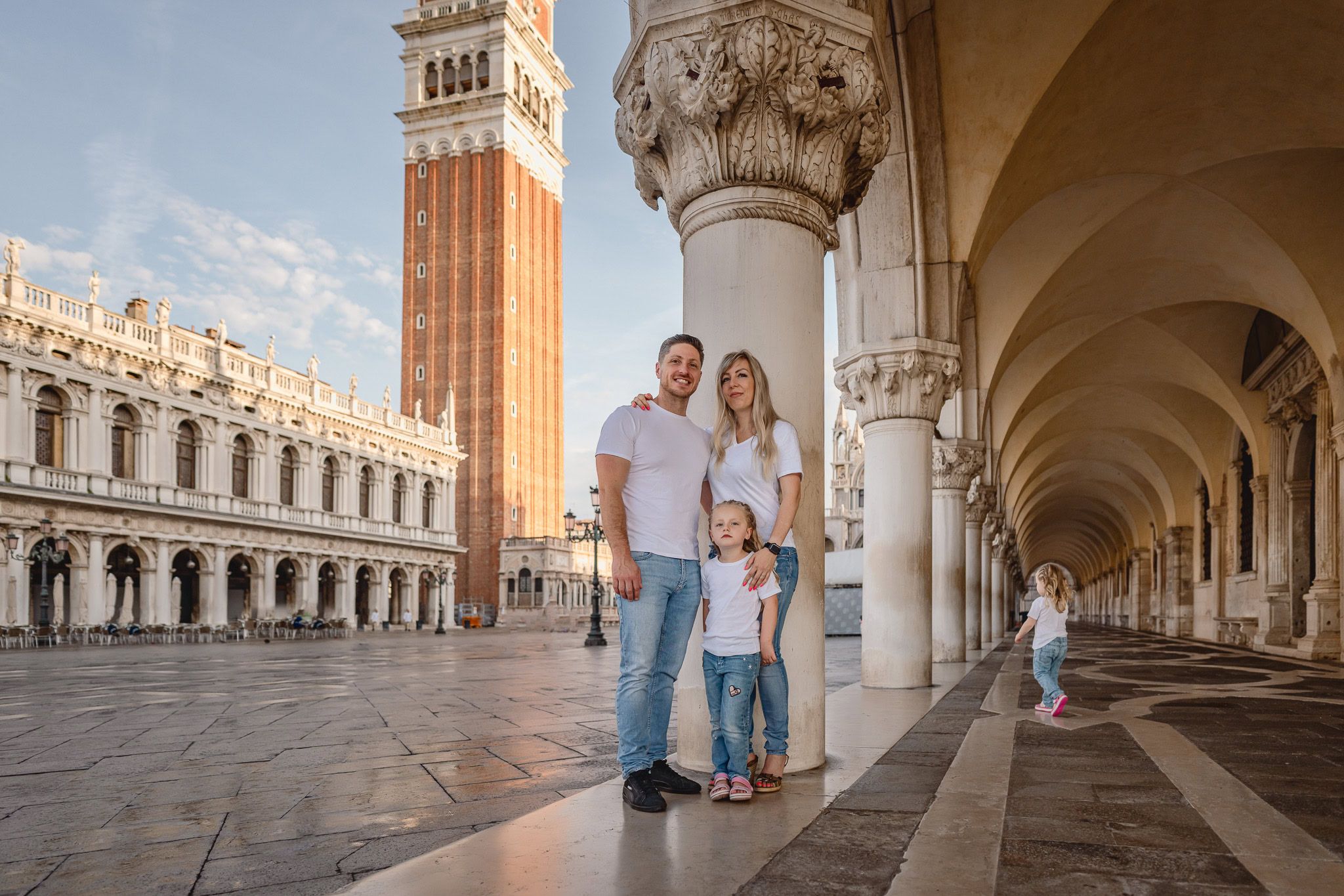 A family of three standing near columns in Piazza San Marco with the Campanile in the background.