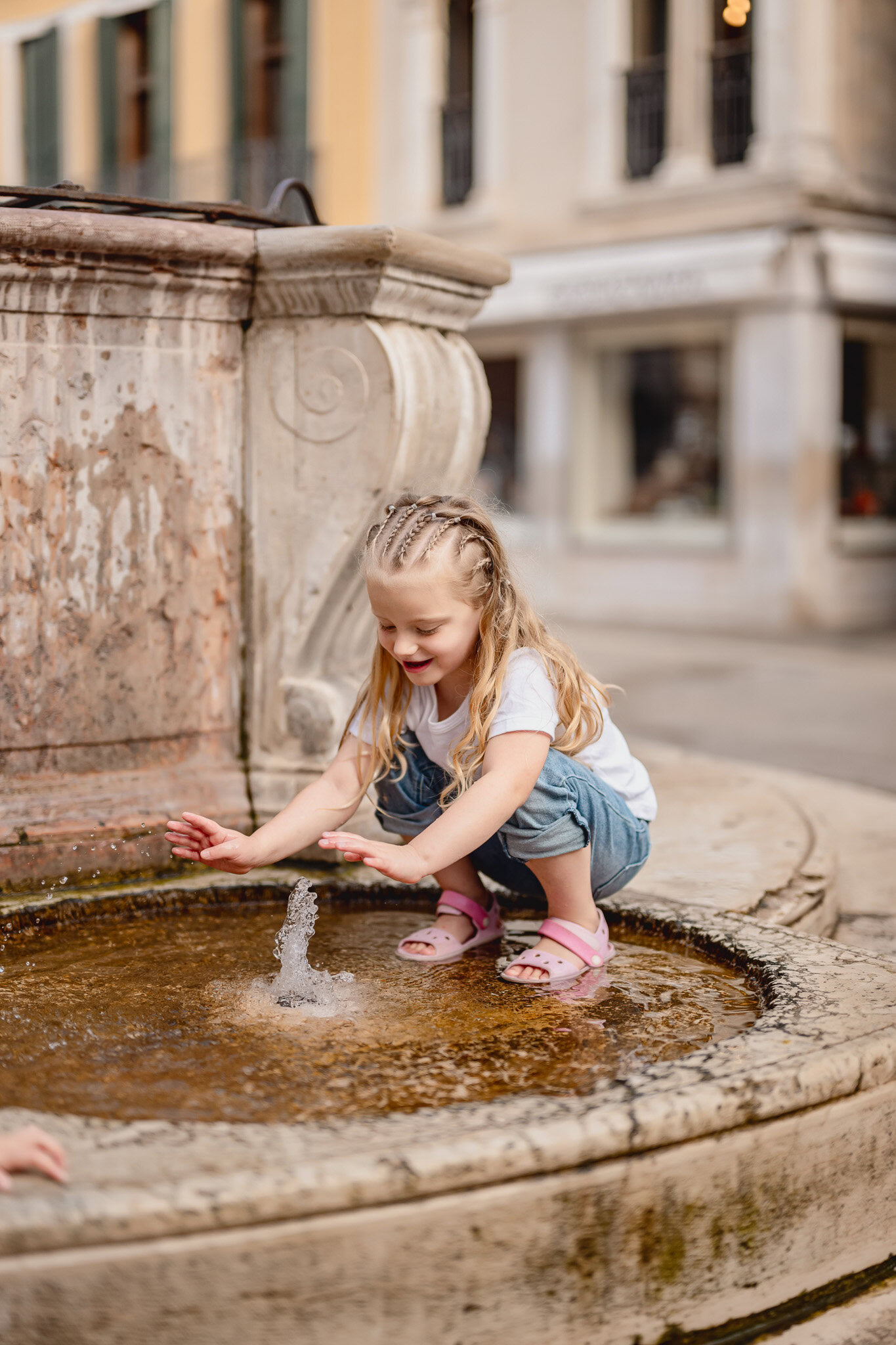 A girl with long blonde hair playing with water at a fountain in San Marco Square, Venice.