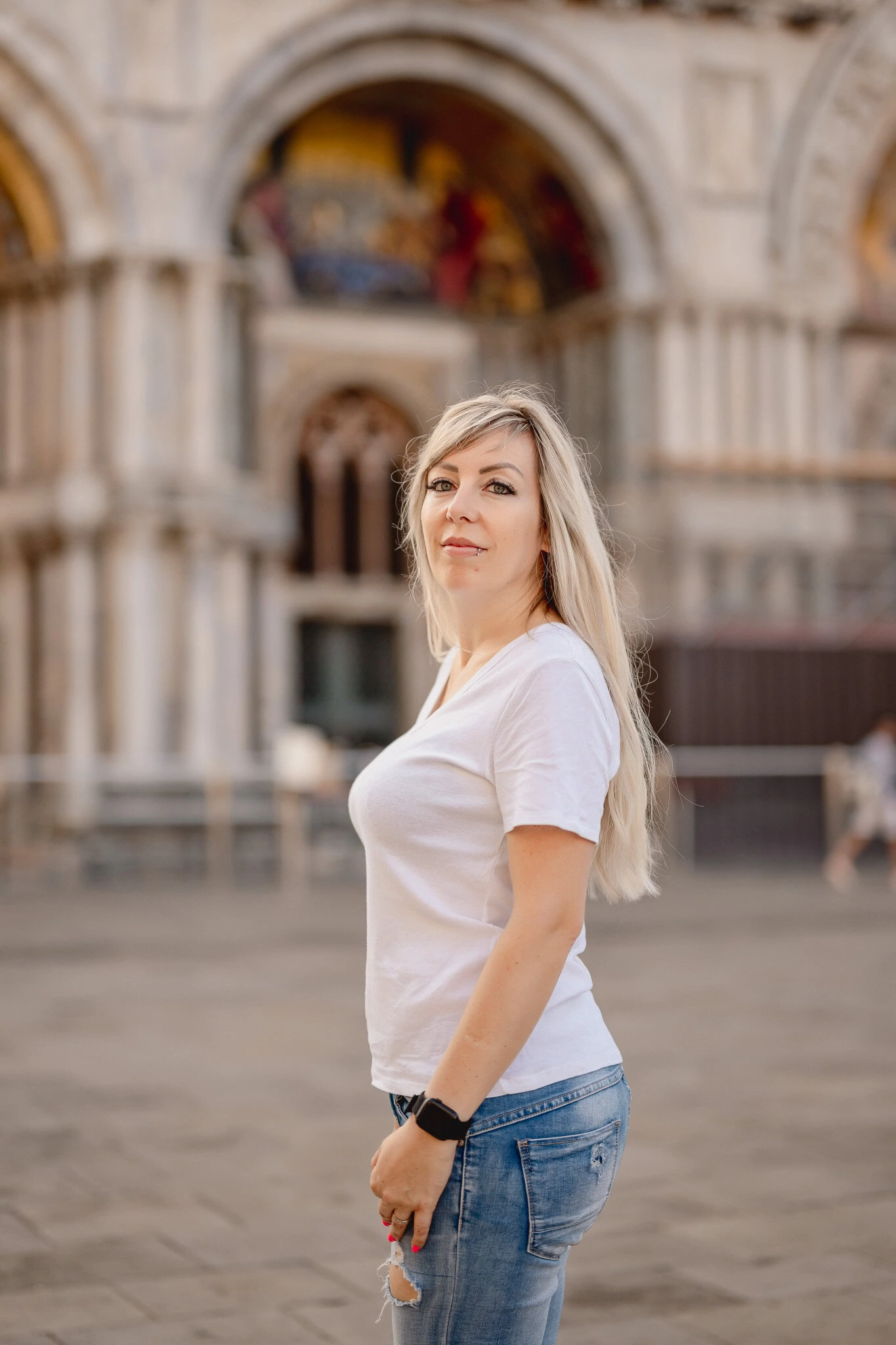 A woman with long blonde hair standing in front of San Marco Square in Venice, Italy.