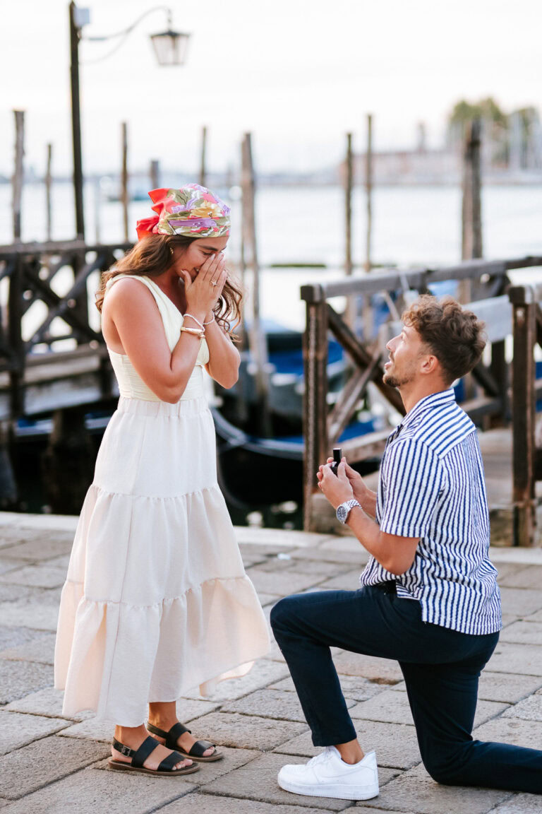 A woman reacts with surprise as a man proposes in Venice at sunrise.