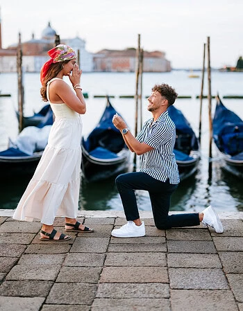 A woman reacts emotionally as her partner proposes in Venice at sunrise.