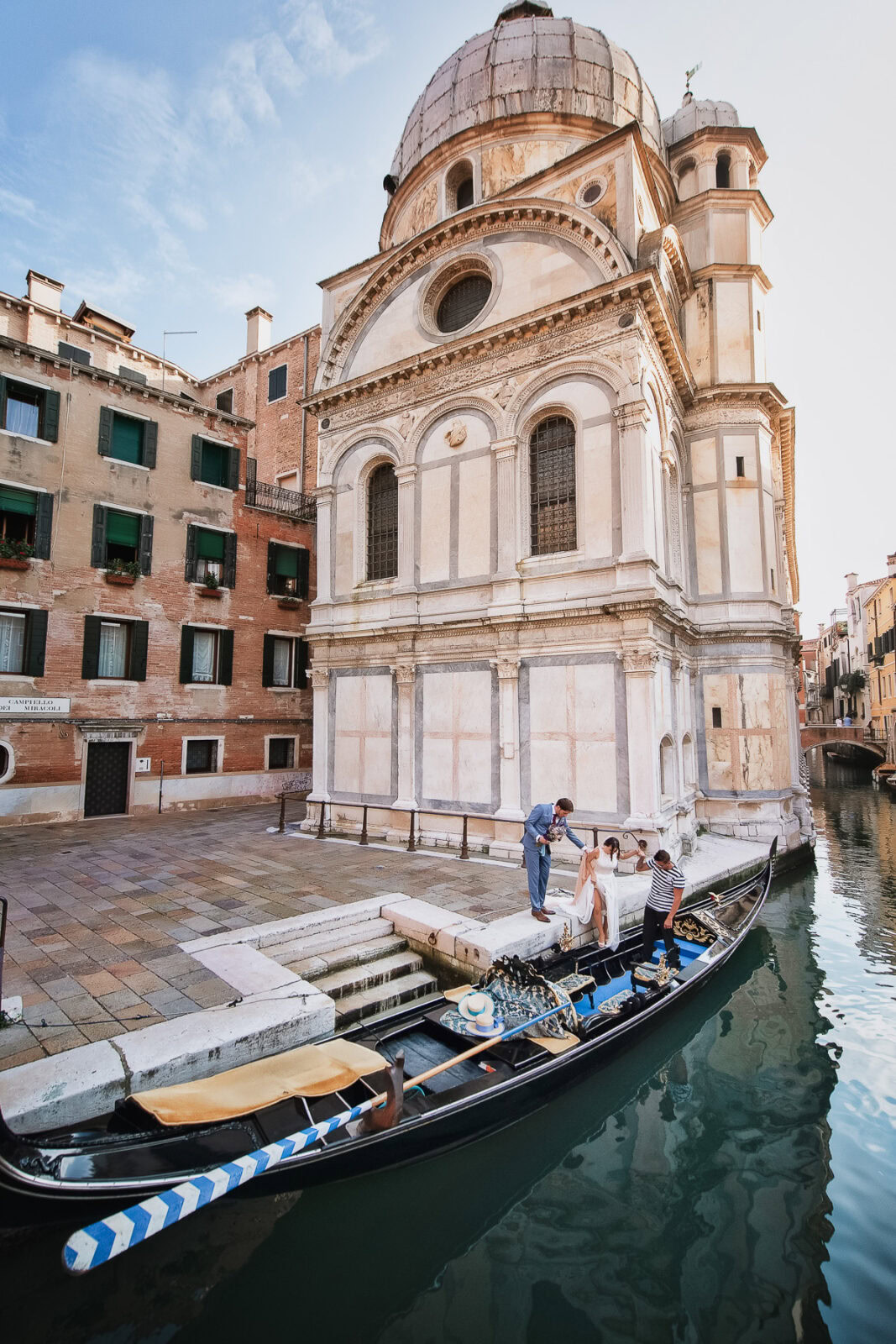 A couple sharing a symbolic gondola elopement experience in Venice, surrounded by water reflections.