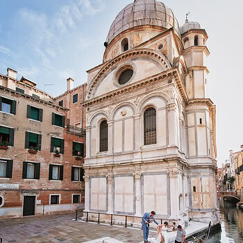 A couple sharing a symbolic gondola elopement experience in Venice, surrounded by water reflections.