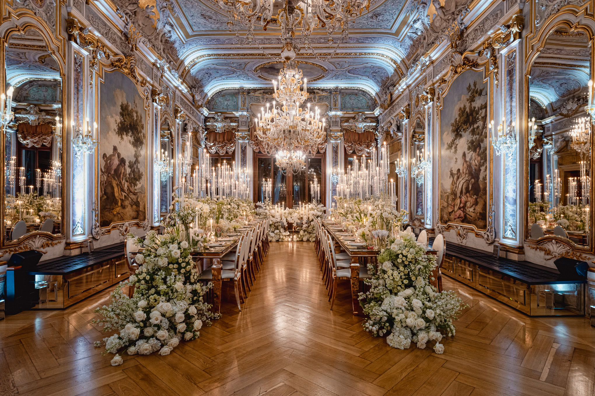 Elegant Venetian wedding reception hall with ornate gold details, grand chandelier, and floral arrangements in soft whit.