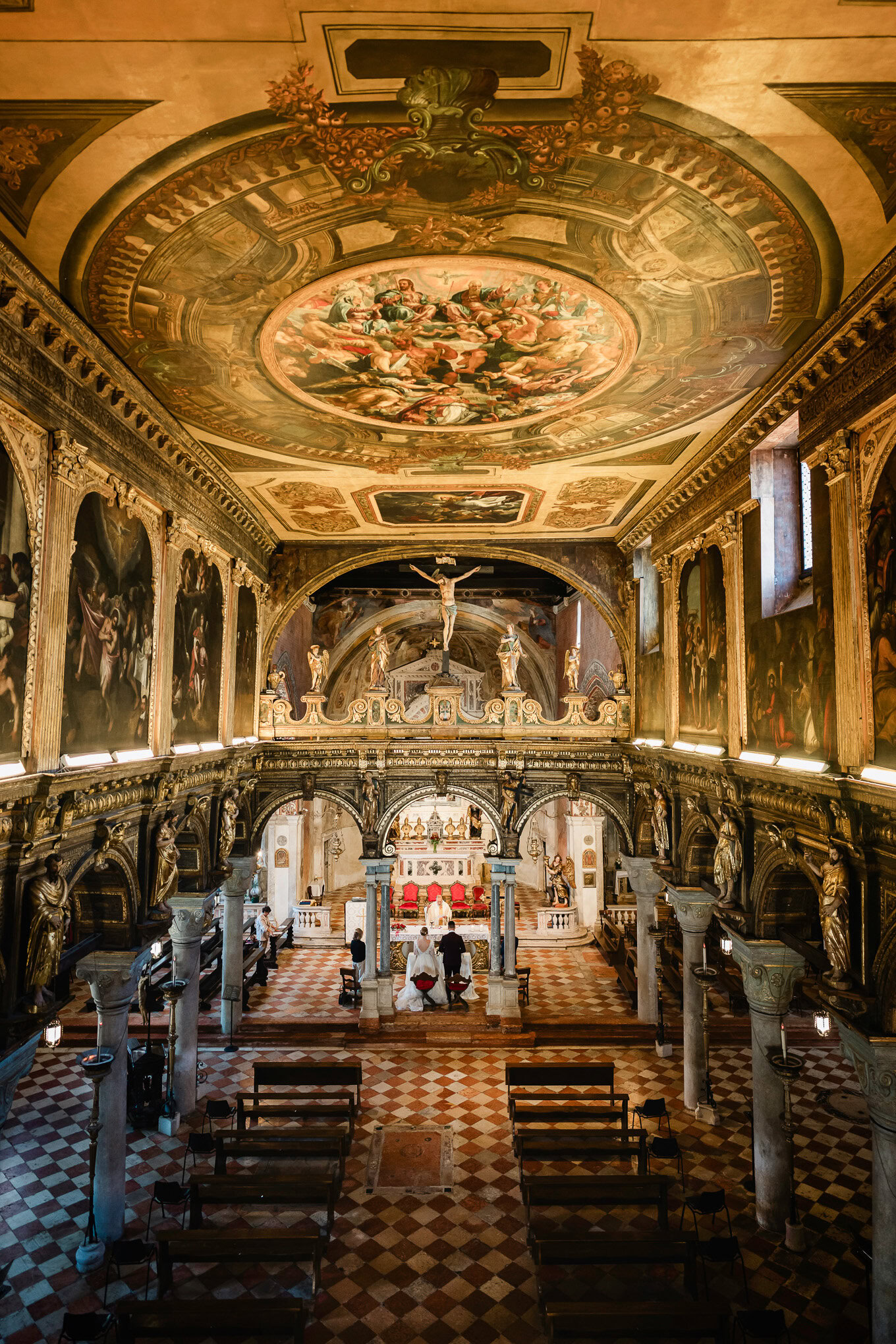 A beautiful wedding scene inside an ornate Venetian church with intricate ceiling frescoes and warm, ambient lighting.