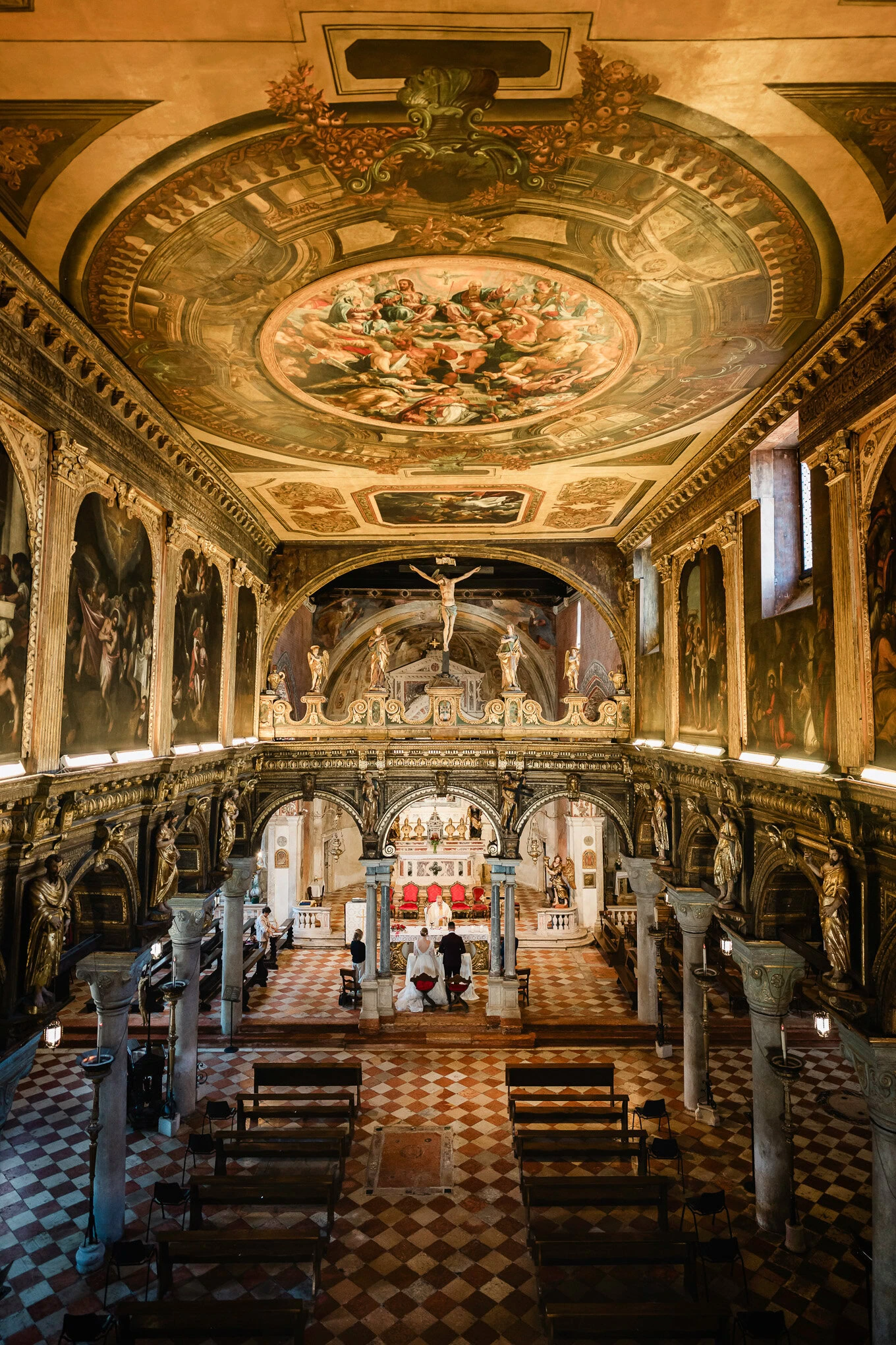 A beautiful wedding scene inside an ornate Venetian church with intricate ceiling frescoes and warm, ambient lighting.