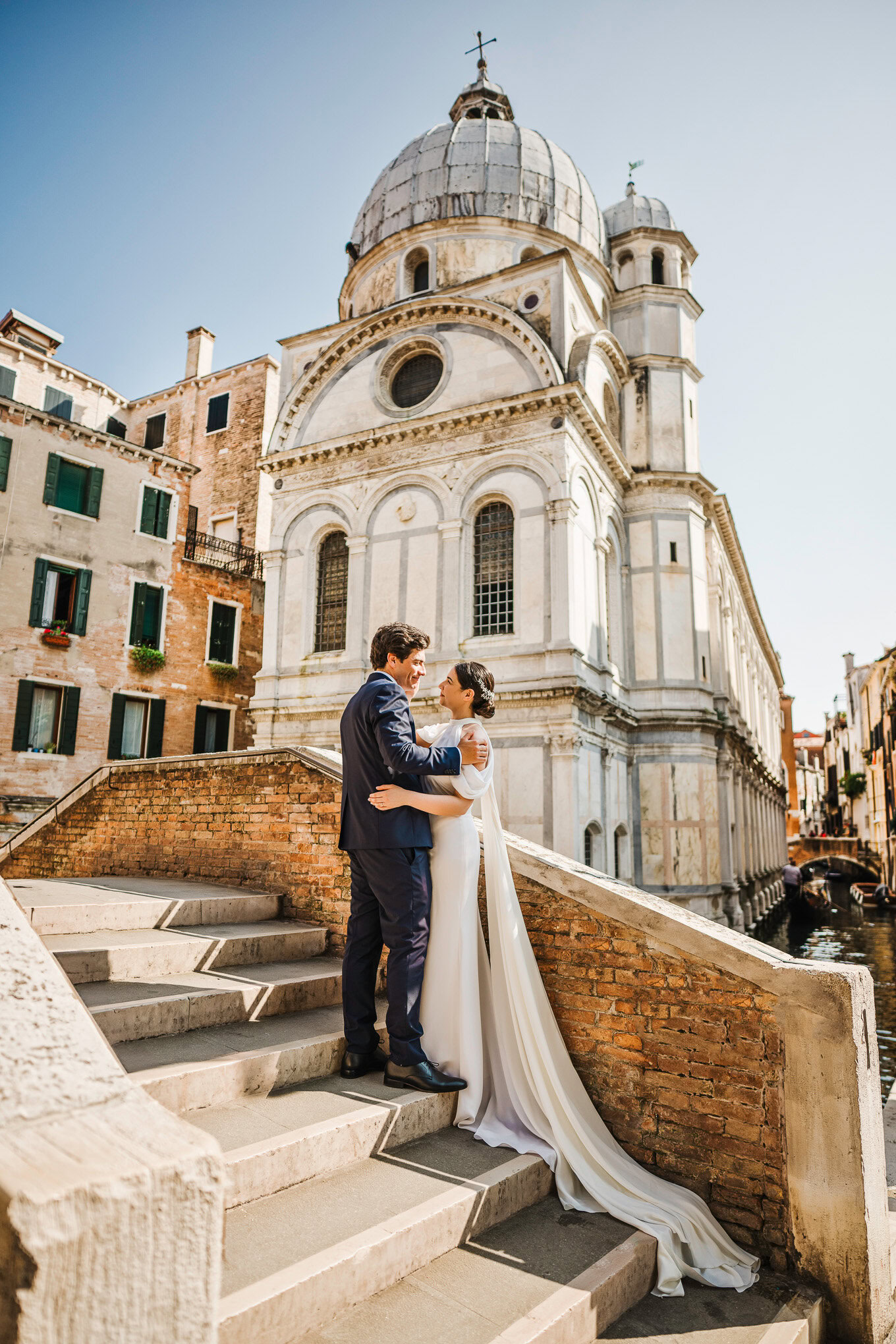 A couple shares an intimate moment on the steps of a historic Venetian church, bathed in warm sunlight and surrounded by.