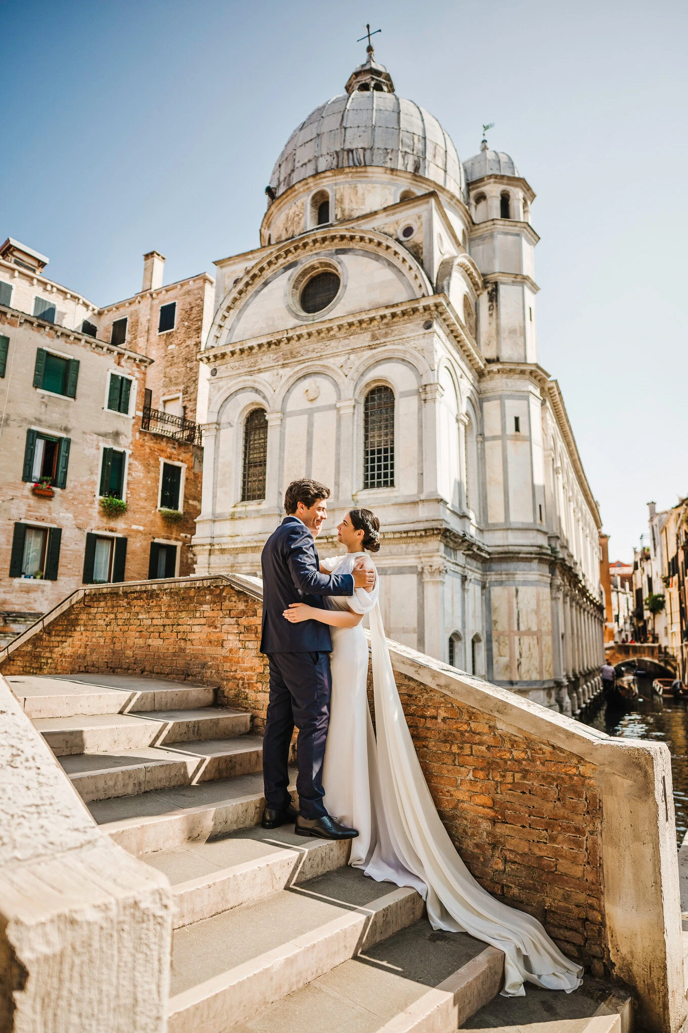 A couple shares an intimate moment on the steps of a historic Venetian church, bathed in warm sunlight and surrounded by.