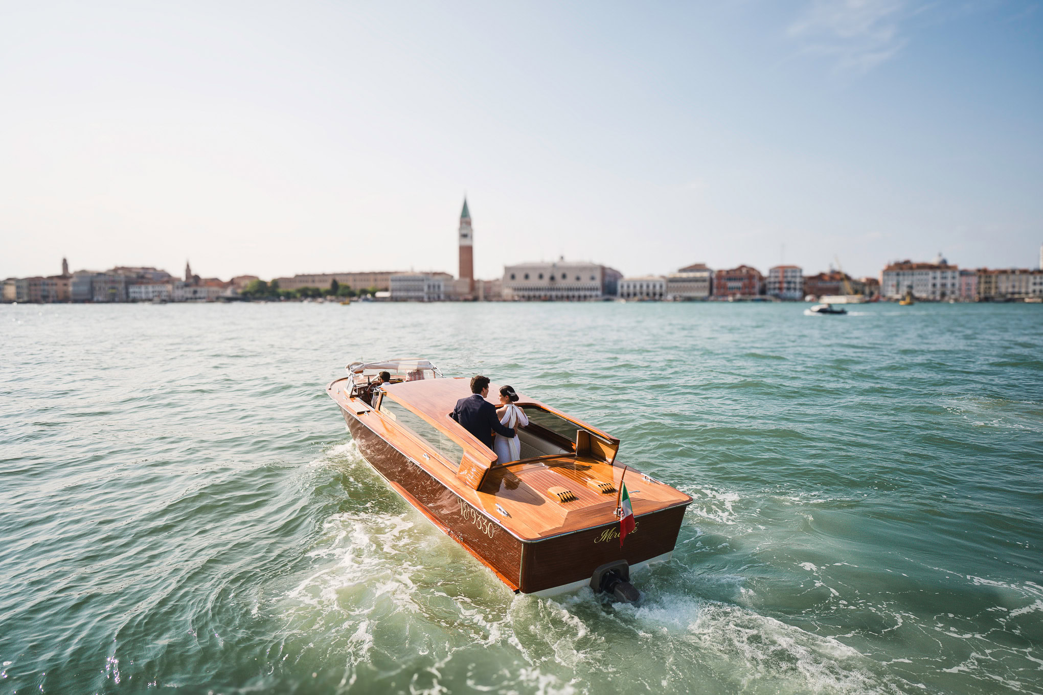 Venetian scene with two people on a boat cruising through the water in Venice.