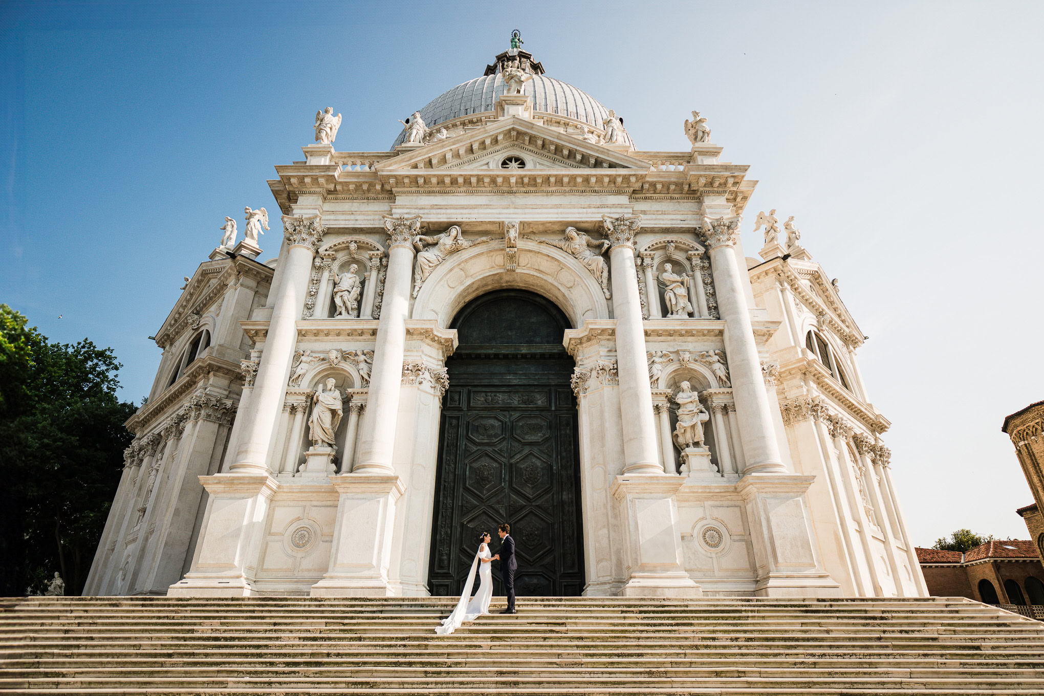 A couple standing in front of a grand Venetian church with ornate architecture and a large dome.
