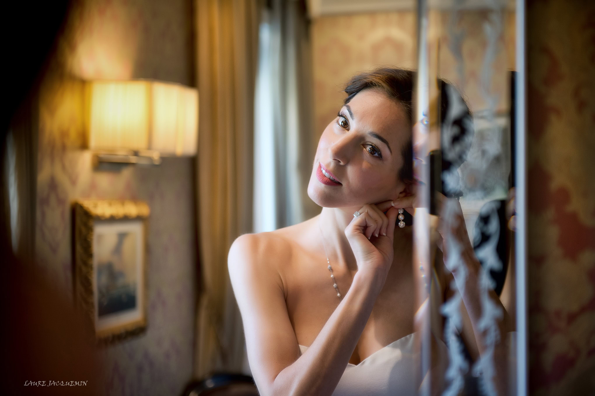 A beautiful bride gazes softly through a window in a warmly lit Venetian interior, capturing an intimate and elegant wed.