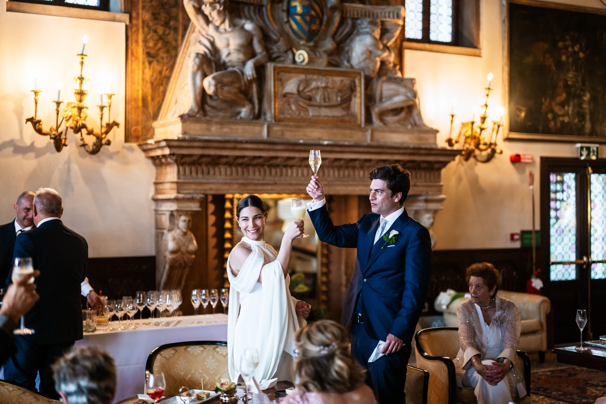 Elegant newlyweds share a joyful dance in a historic Venetian ballroom illuminated by warm candlelight and ornate chande.