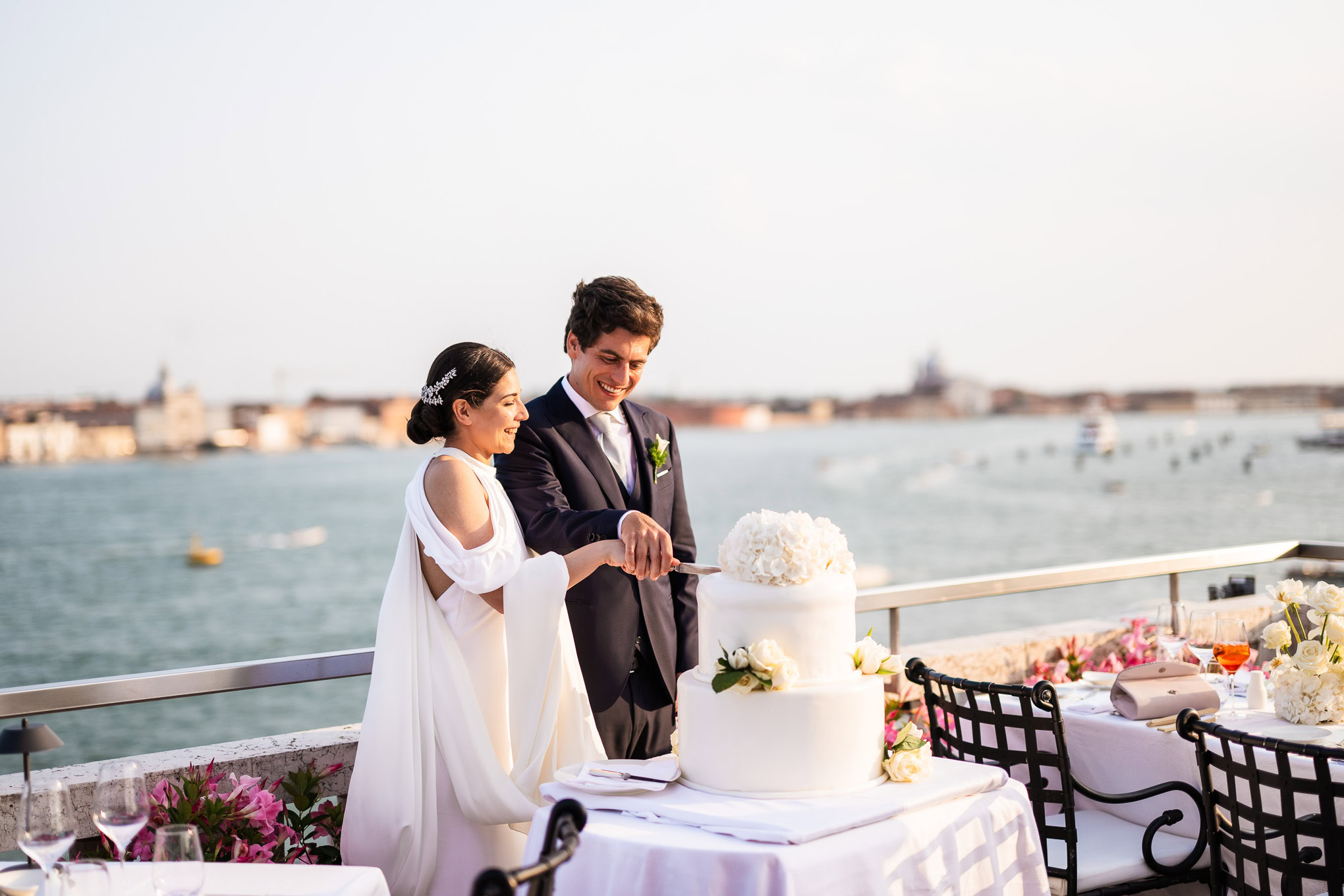 A couple cutting a wedding cake with Venetian waterfront in the background.