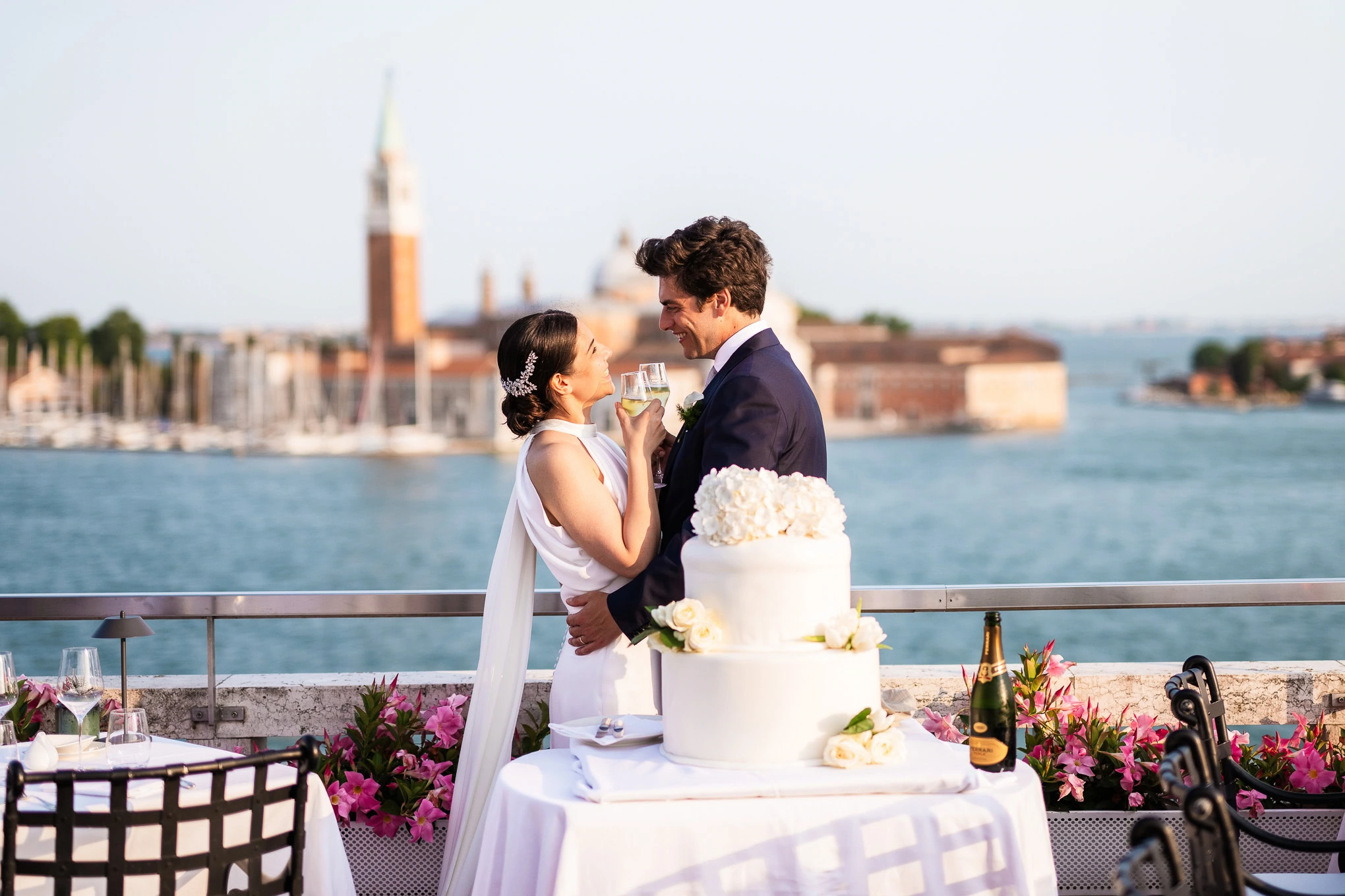 Romantic Venice scene with a couple celebrating outdoors by the water during golden hour, featuring a cake and s.