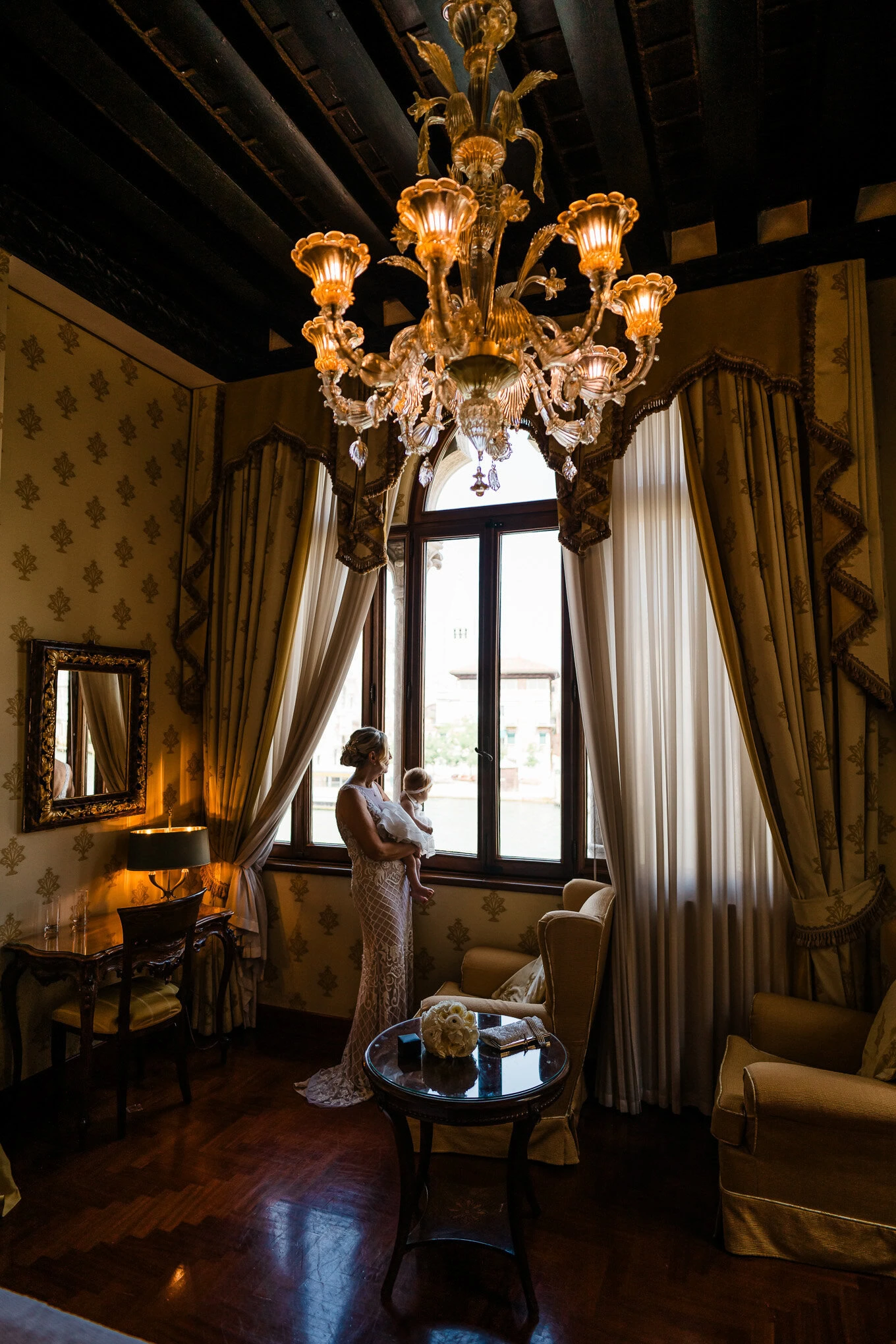 A woman in an elegant dress stands by a large window in a luxurious, vintage Venetian interior illuminated by a.