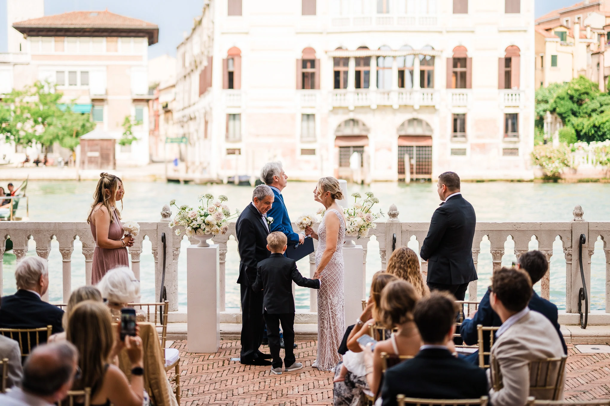 A woman and man exchange vows during a wedding ceremony by the Venice canal, with elegant attire and soft natural light.